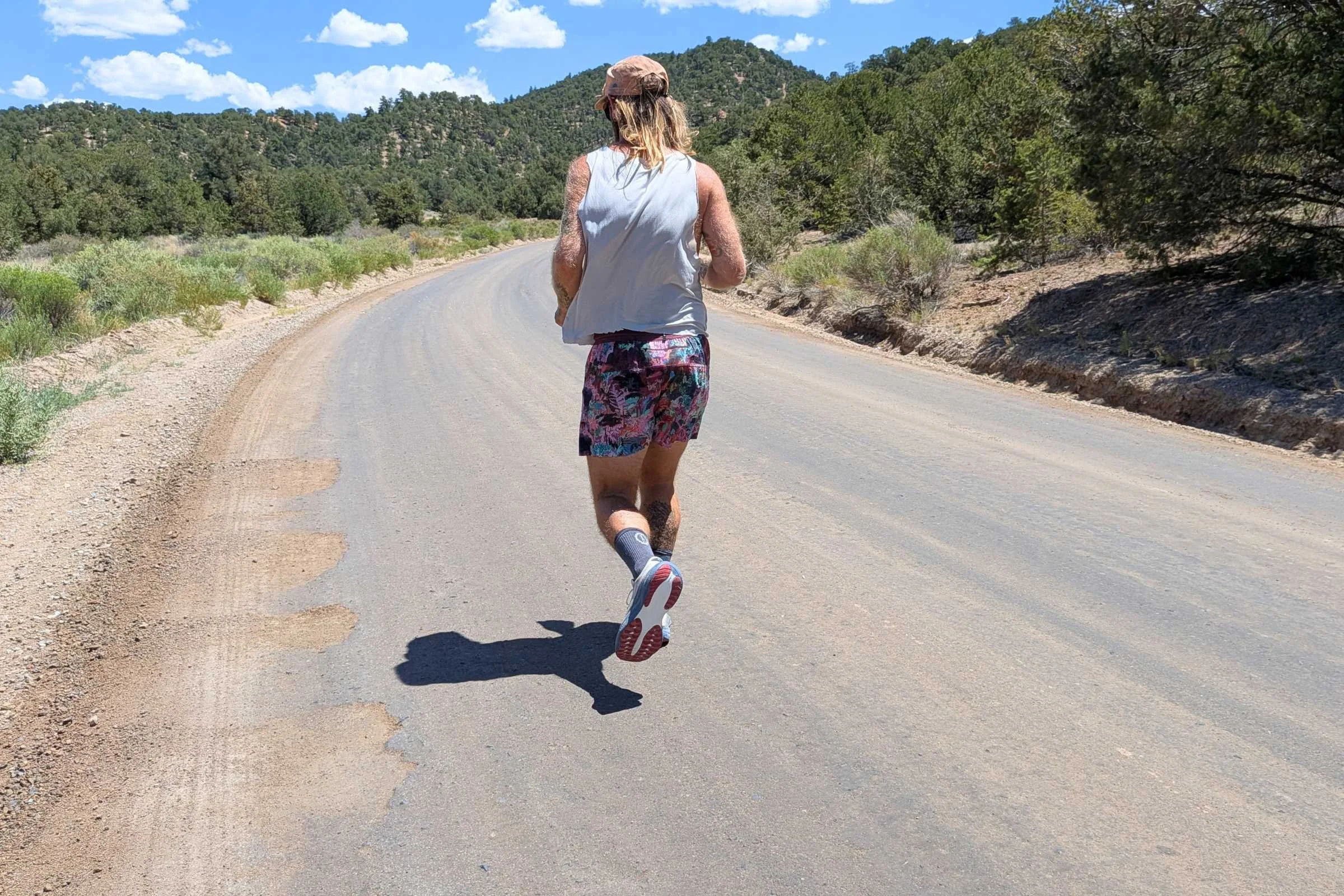 A man wearing Janji AFO Middle Running Shorts runs along an empty road.
