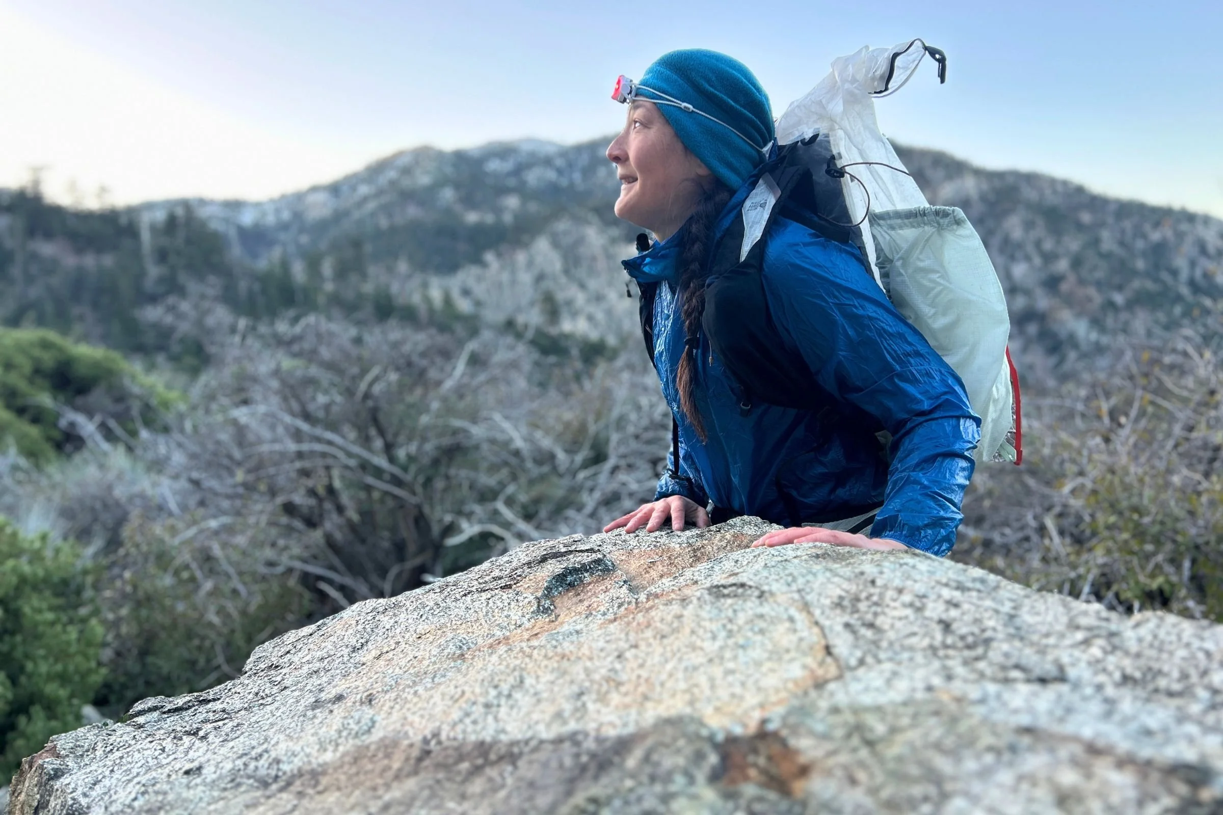 The author, wearing a backpack, standing next to a large boulder, wearing the Petzl Swift LT headlamp in red light mode.