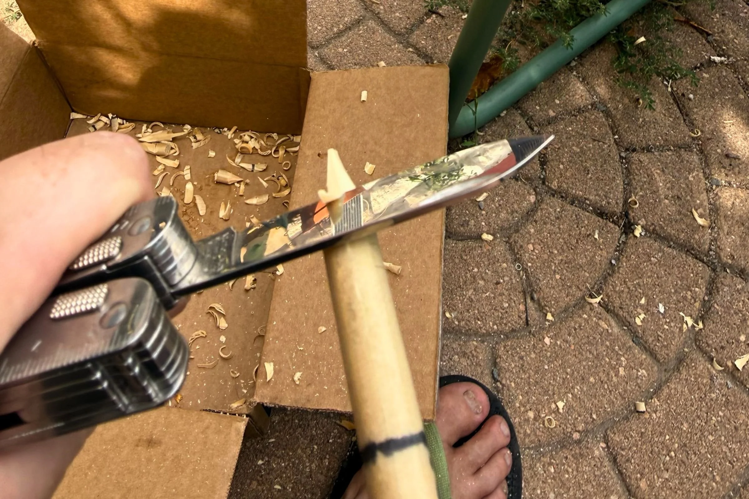 Using the Victorinox Swiss Tool X blade to carve a wooden dowel into a tent stake.