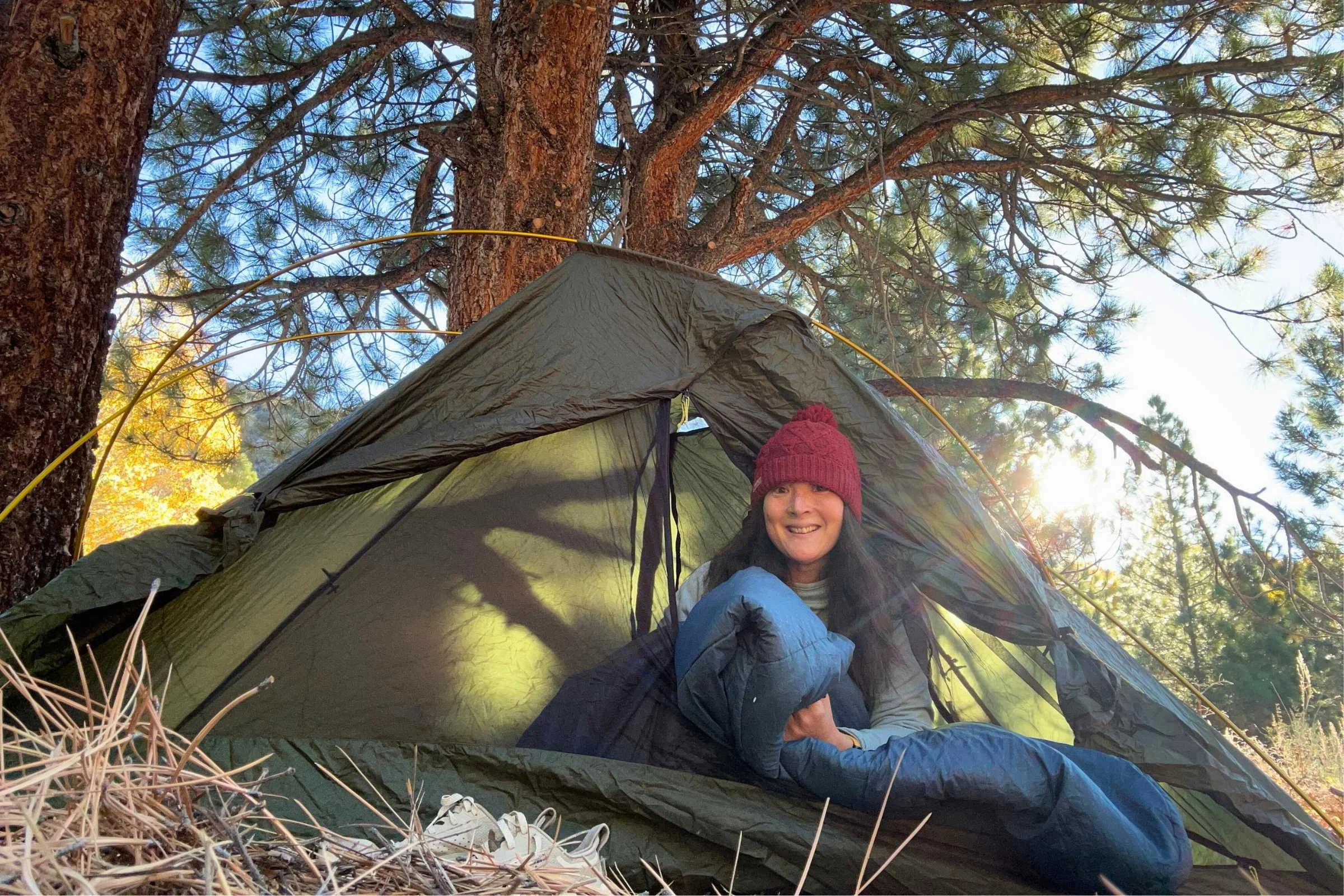The author sitting in a blue Exped DeepSleep sleeping bag outside her tent in the woods