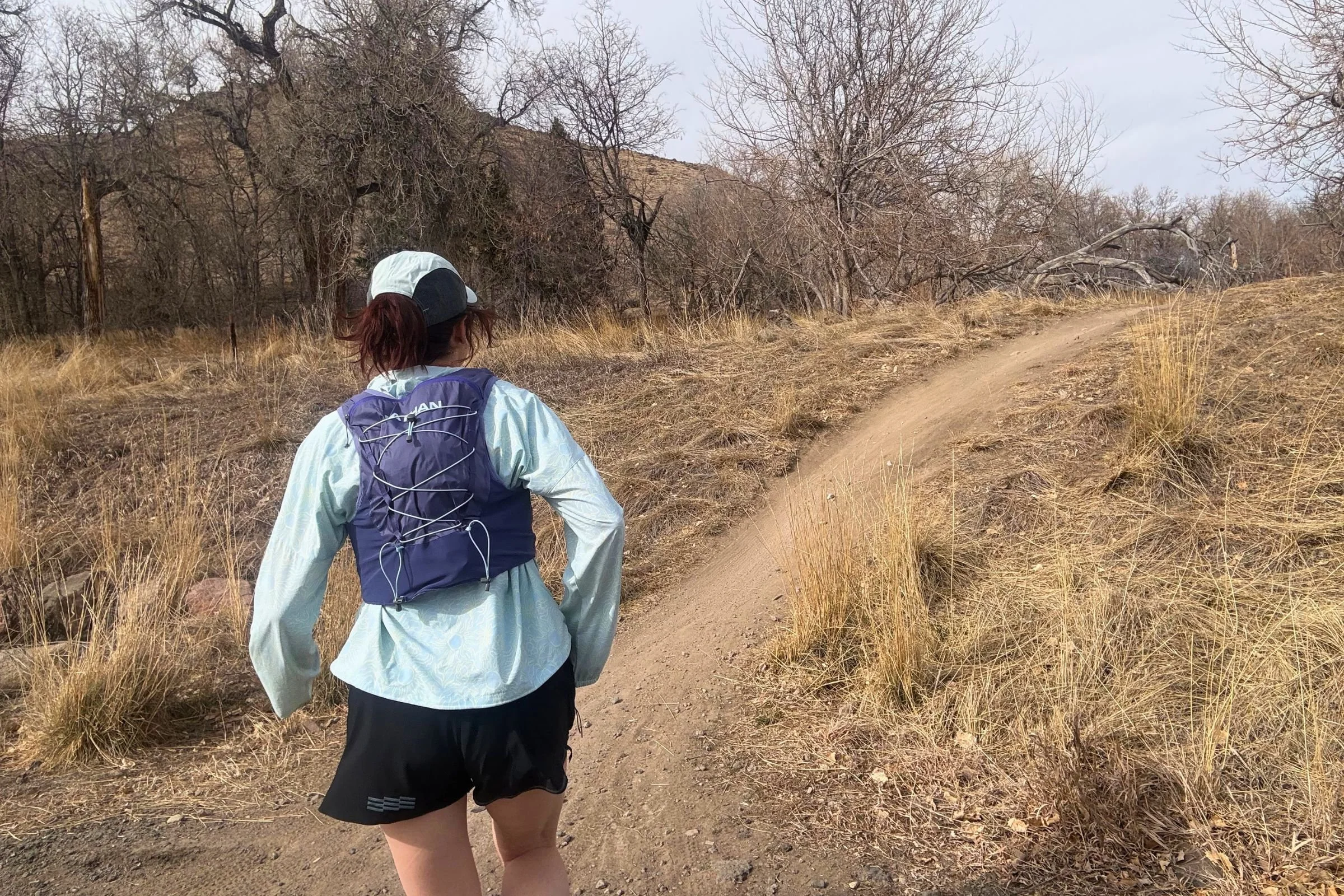 Woman running along a daytime trail while wearing a Nathan VaporAir pack.