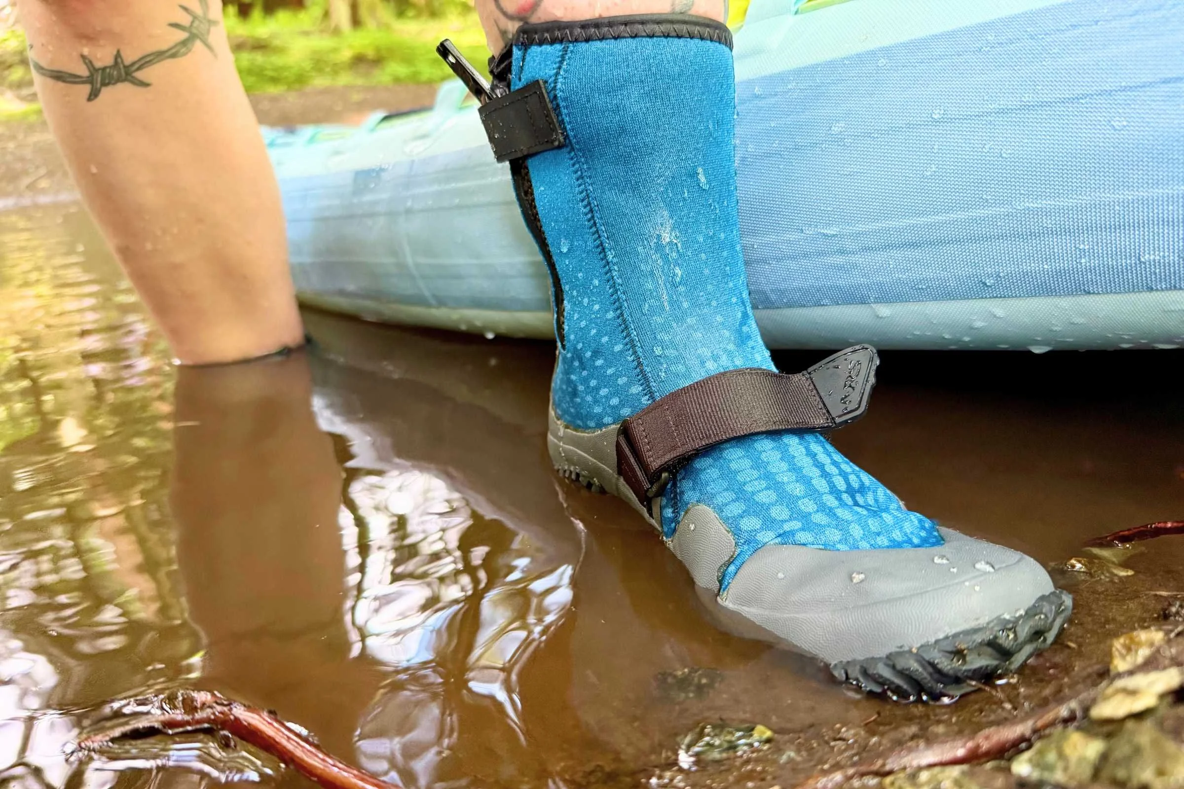 Person wading in the water in the NRS Paddle Wetshoe next to a paddleboard