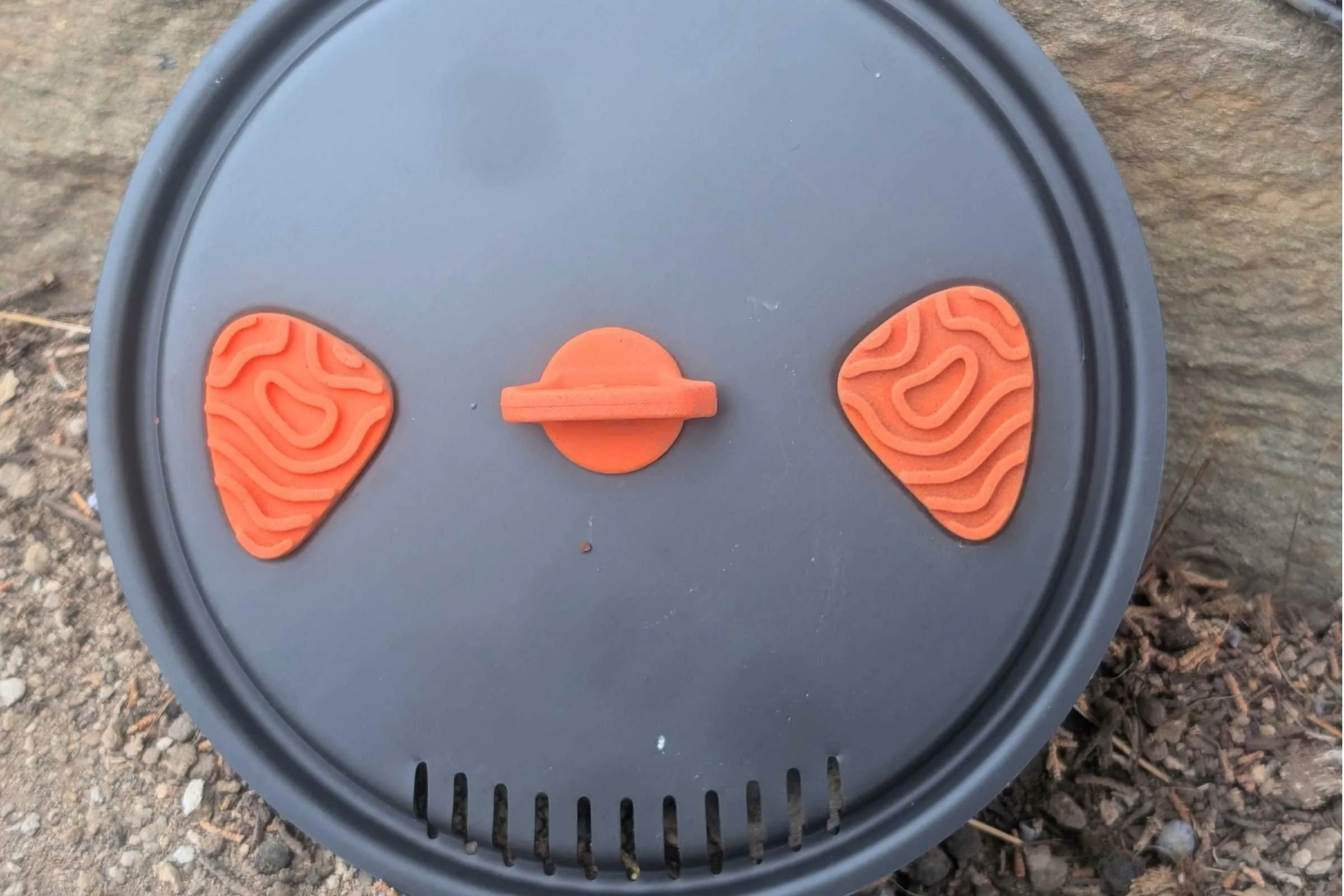 A close-up view of the top of the lid featuring the rubberized handle and two touch points for using the spout (not pictured) and strainer.