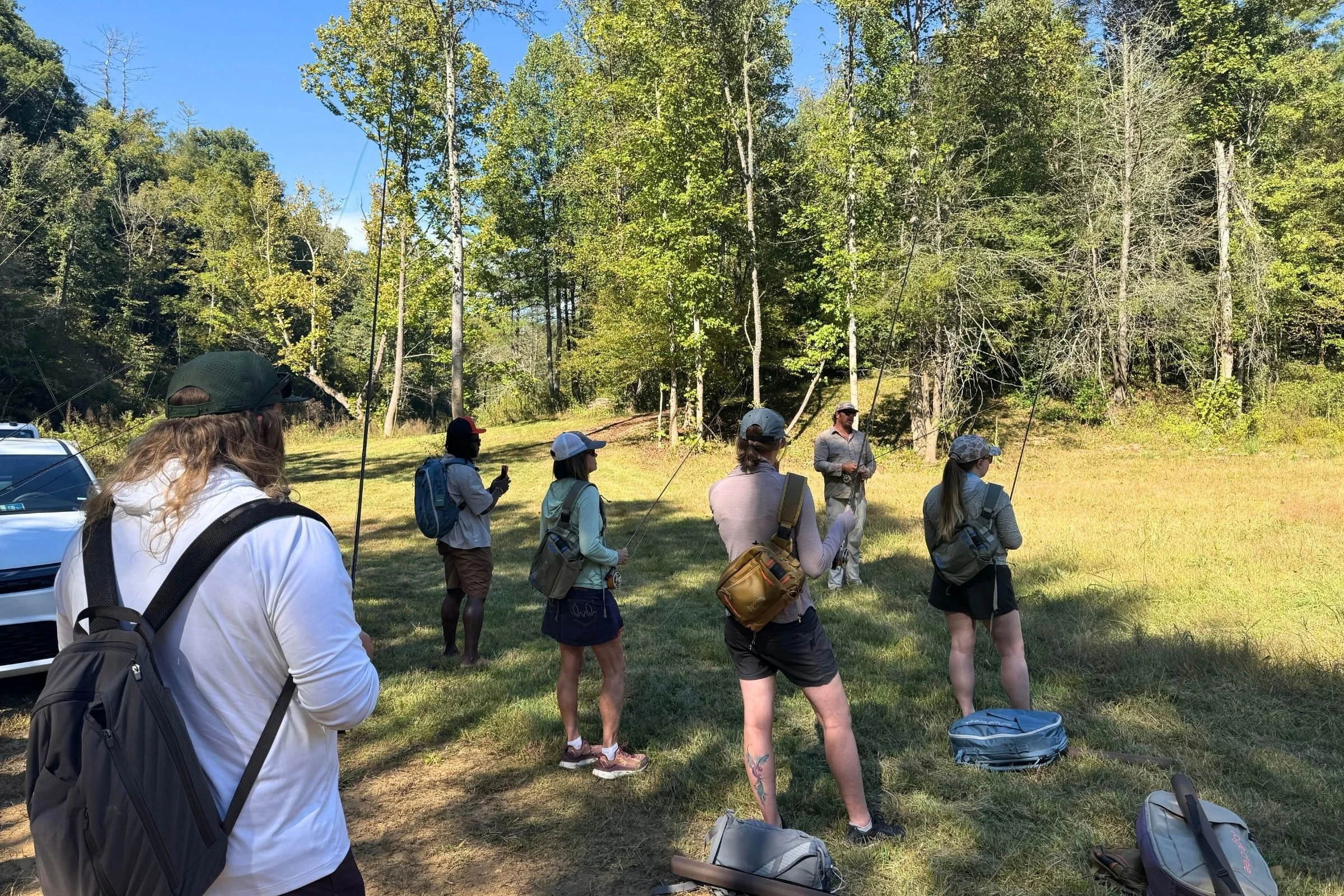 A group gathers in a field beside a car during an outdoor excursion at the 2026 Outdoor Media Summit.