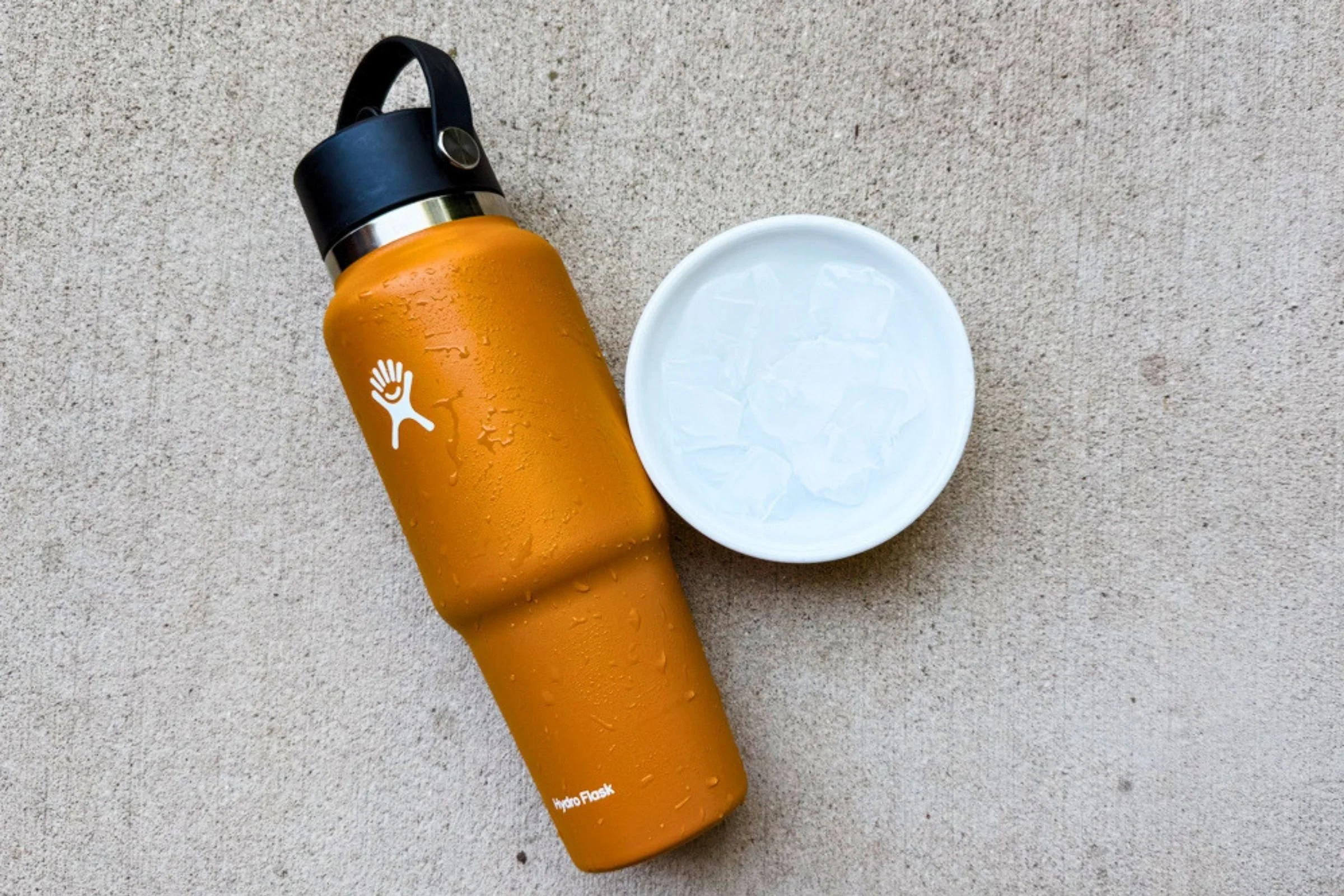 Orange Hydro Flask 32 oz Travel Bottle beside a bowl of ice, showcasing insulation and condensation resistance.