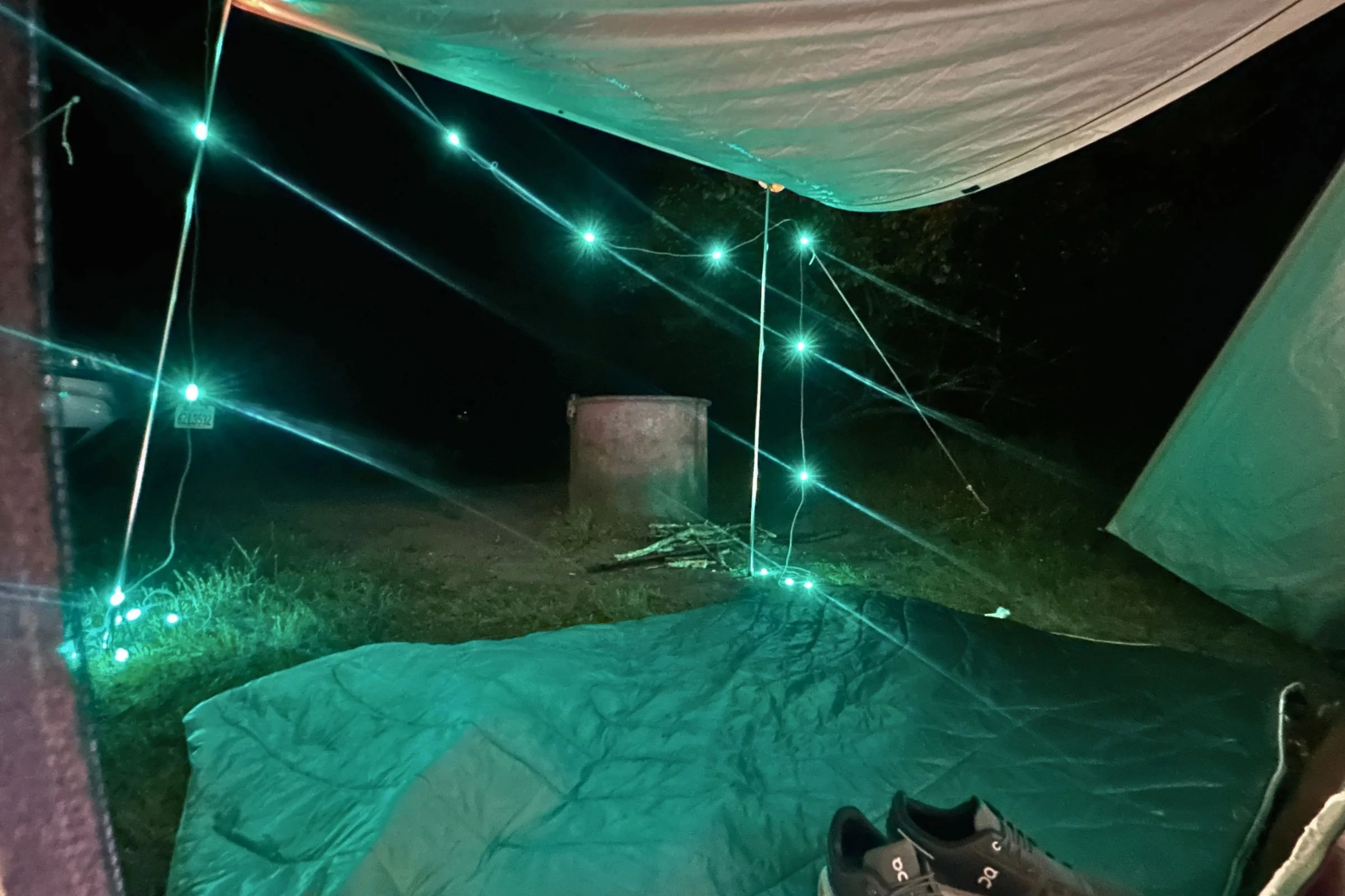BioLite Luci 44' Solar String Lights glow green beneath a camping tent’s awning.