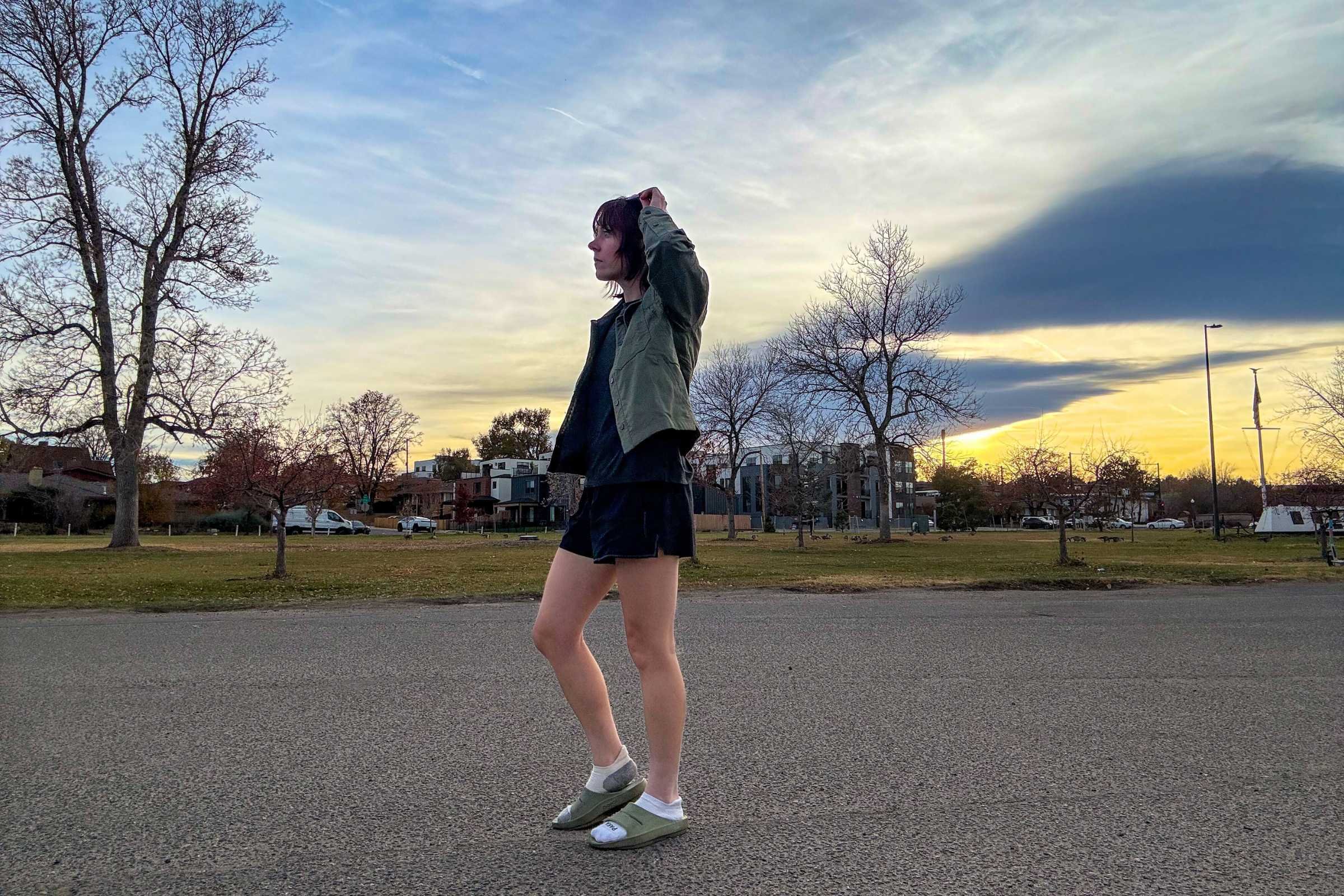 Person walking on a paved path at sunset wearing OOFOS Ooahh recovery slides in a park setting