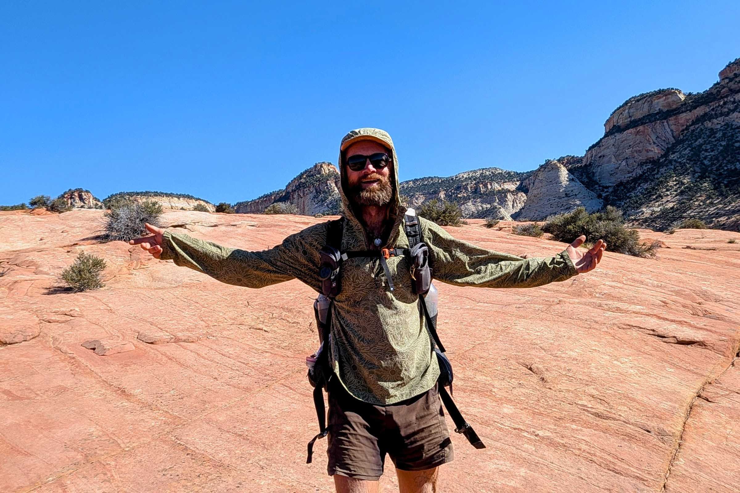 author Sam Schild wearing a green Royal Robbins Salathe Hoodie on a sun-exposed rock slab