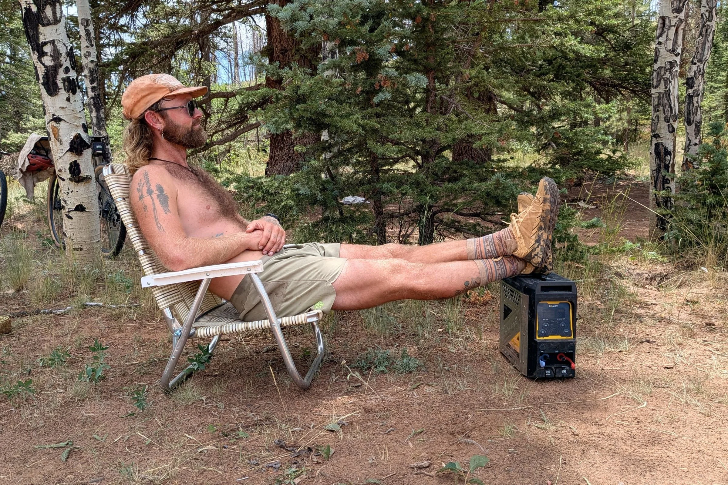 BougeRV Portable Propane Outdoor Water Heater outdoors in the woods beside a person sitting in a chair.