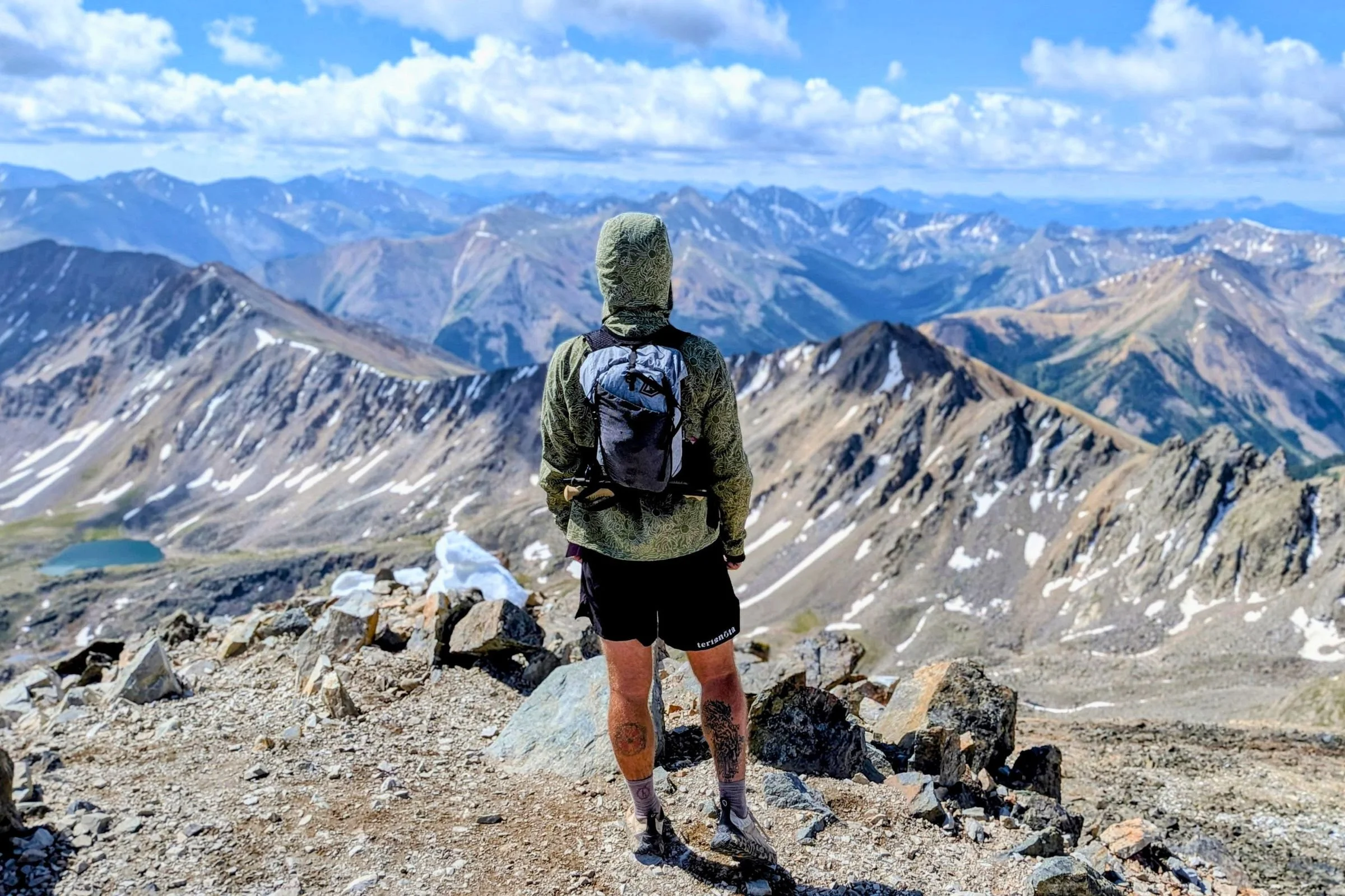 Man wearing a backpack and Terignota Sendero Shorts while standing on a mountain peak.