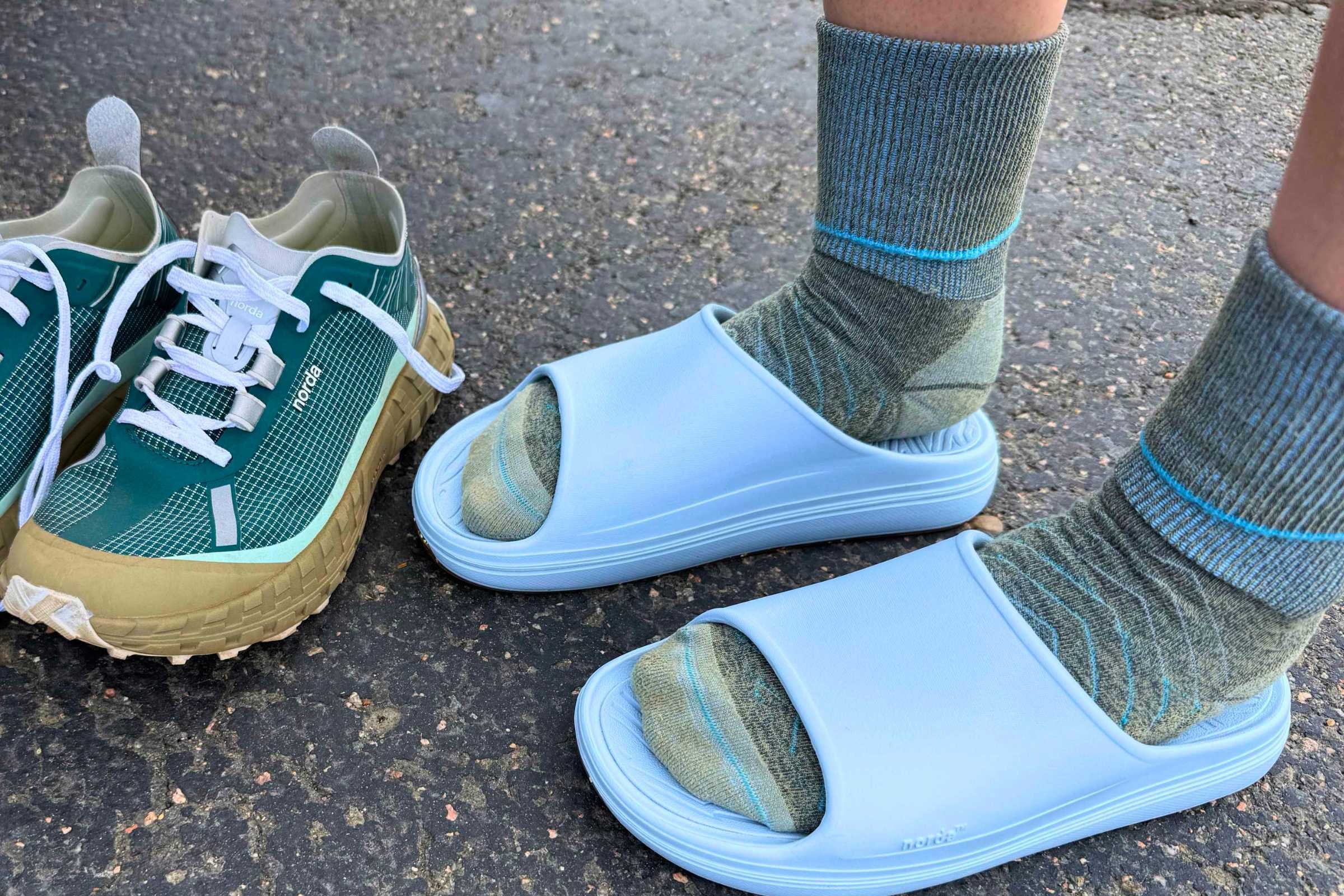 Norda 008 Recovery Slides: A person wearing slides with sneakers beside them.