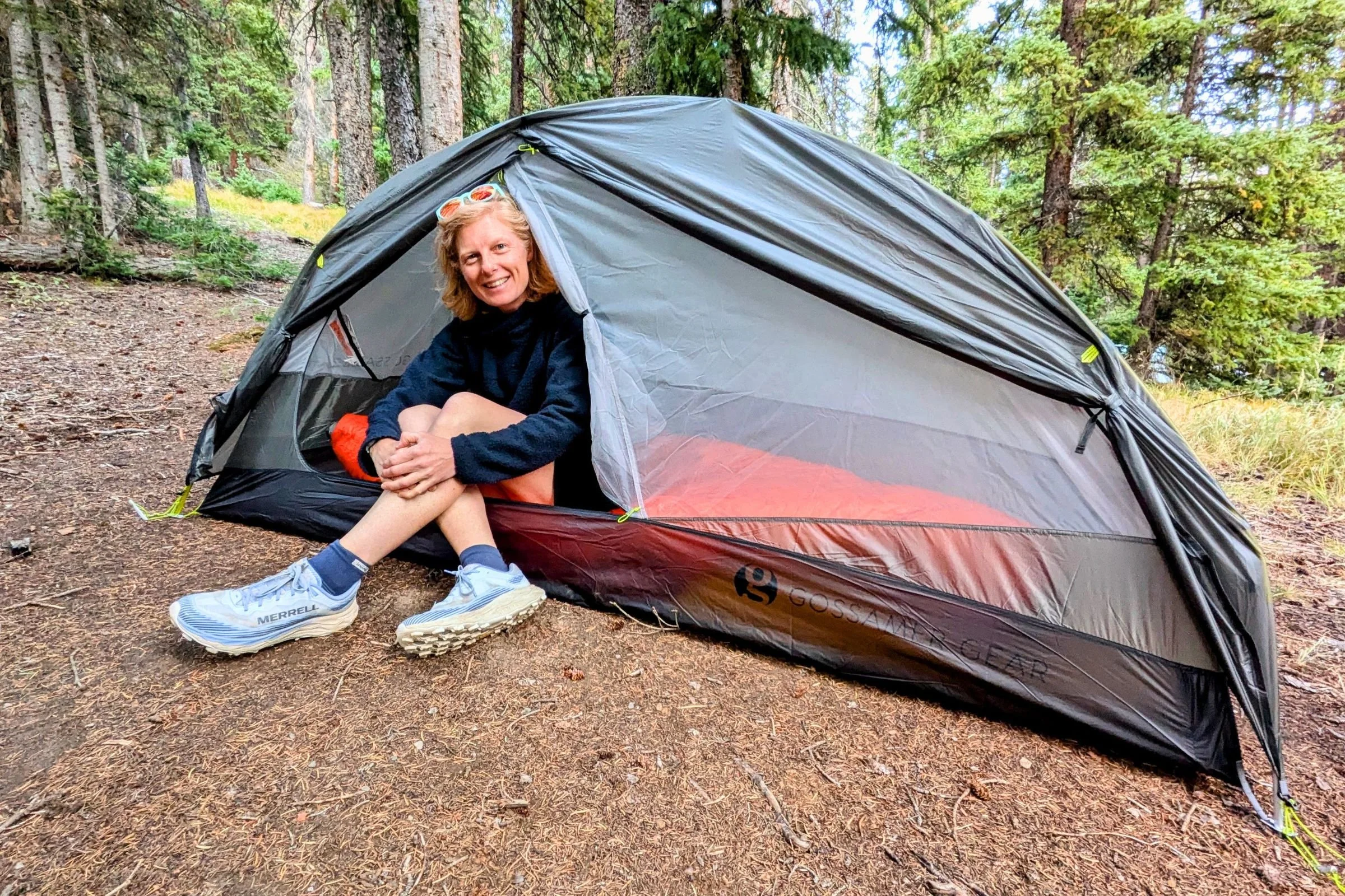 A tester sits in the open doorway of Gossamer Gear The Free at a forest campsite