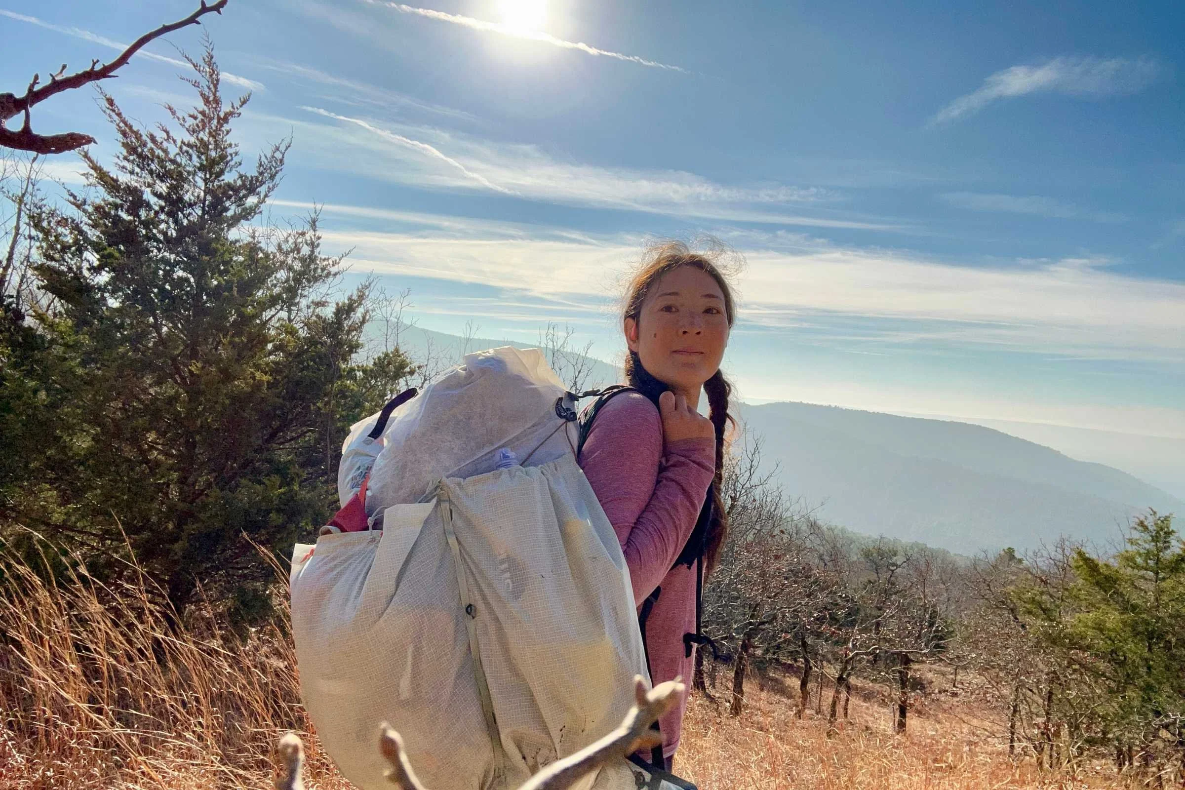 the author backpacking with the mountain hardwear alakazam pack on a sunny day with trees and mountains in the background