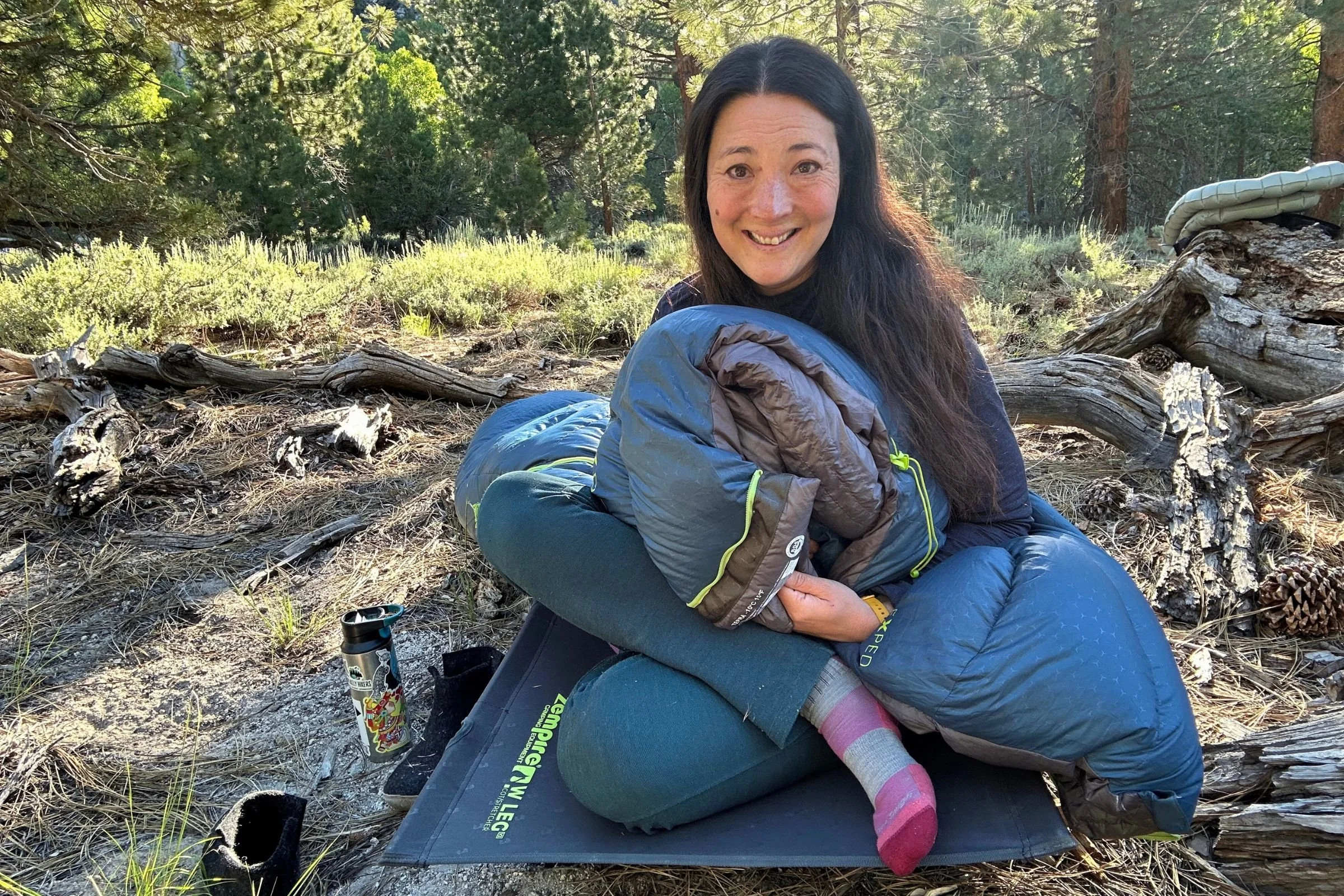 A woman sits on the ground with an Exped Terra Sleeping Bag outdoors.