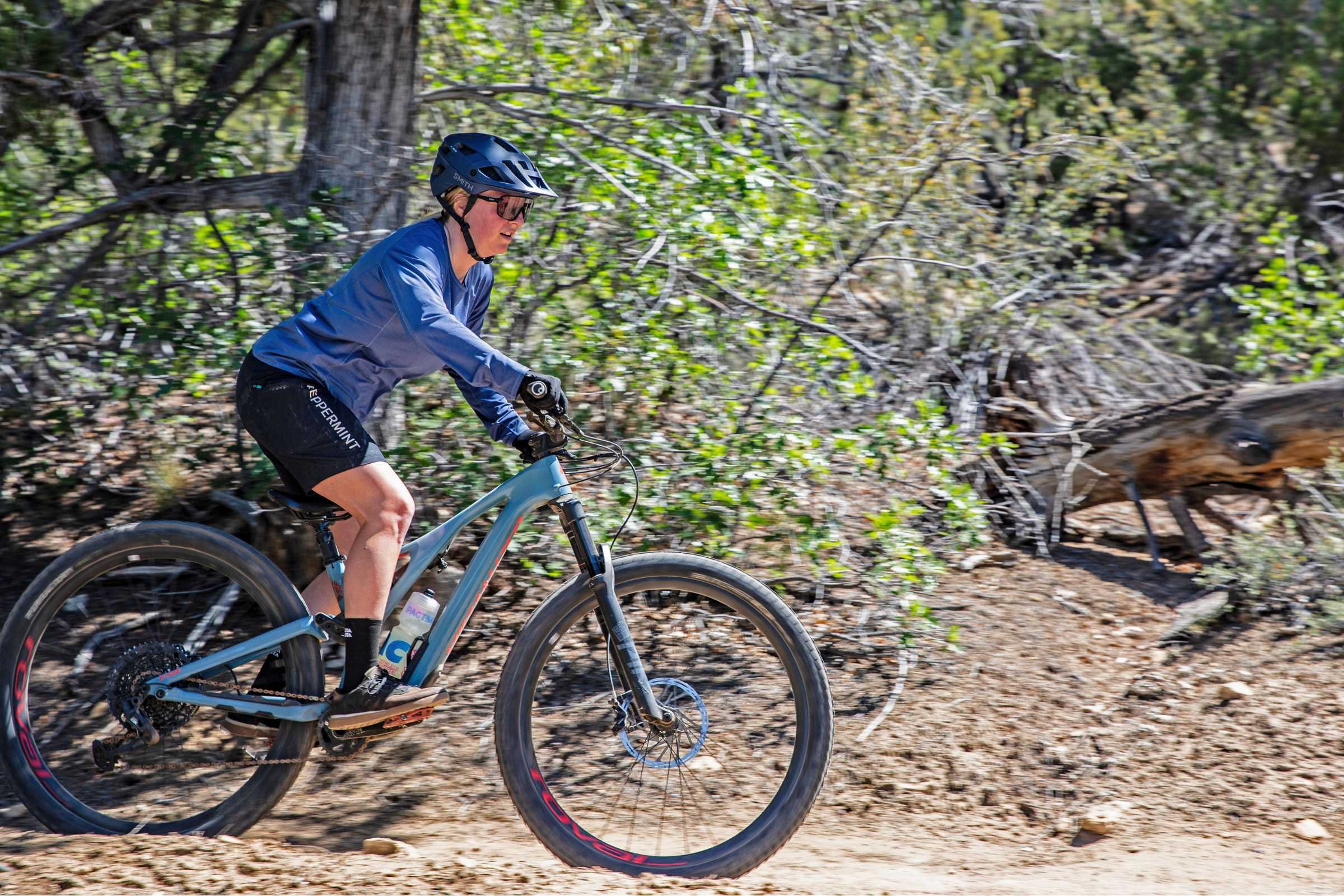 A woman riding a mountain bike wearing the Smith Engage MTB helmet with trees in the background.