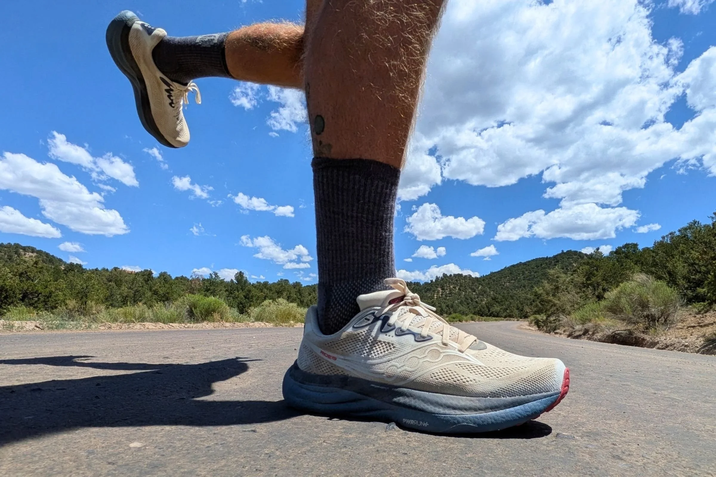Saucony Ride 19 Road Running Shoes worn on a paved road with trees and hills in the background.