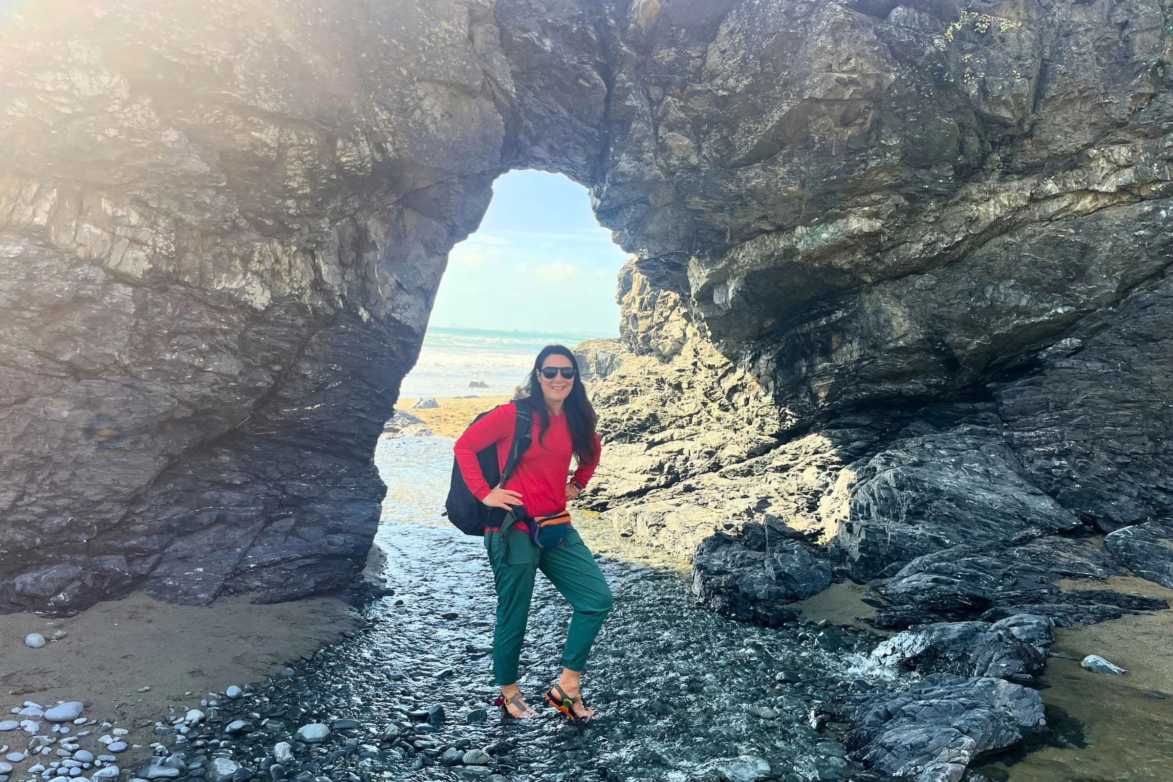 Hiking on the beach through a natural arch wearing the Title Nine Upland Long Sleeve Sun Shirt.