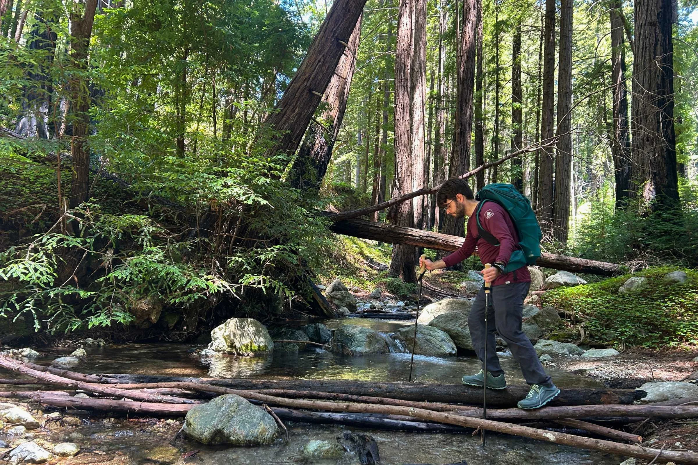 A tester crossing a creek on logs and using the Gossamer Gear FT3 poles for balance