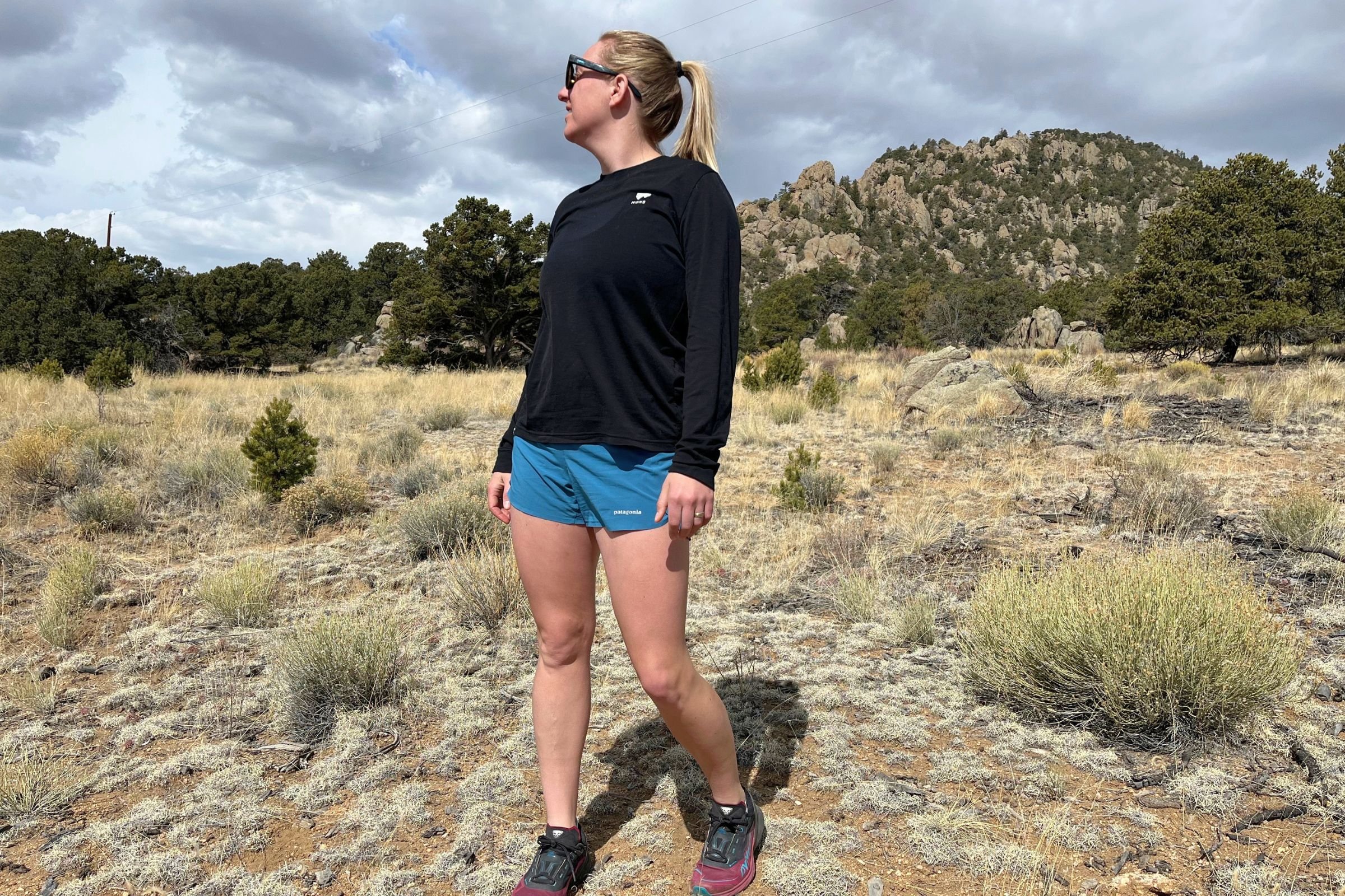 Woman in a black shirt and Patagonia Strider Pro shorts standing in the middle of a field.