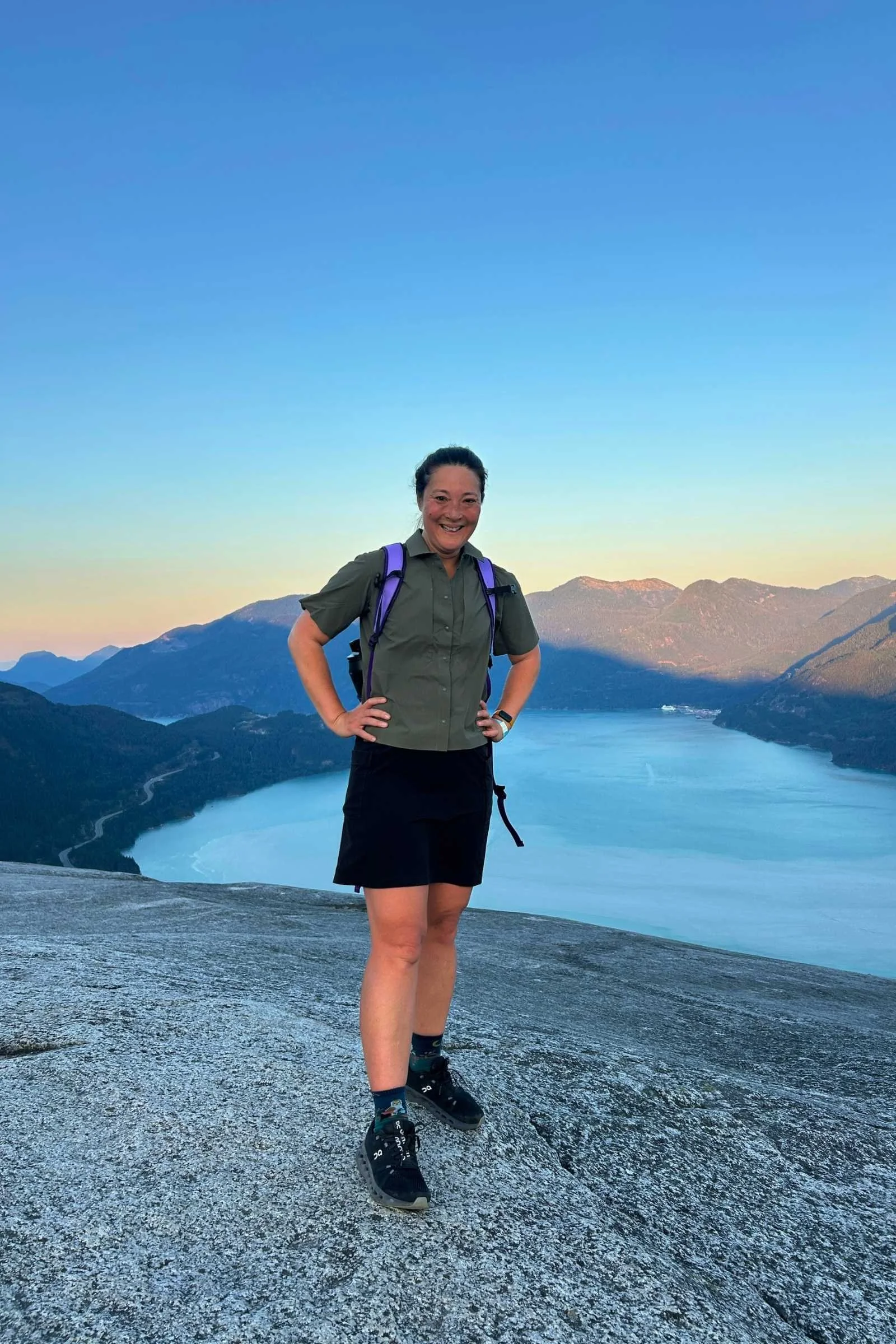 Liz at a summit overlooking an alpine lake wearing the Purple Rain Adventure Skirt