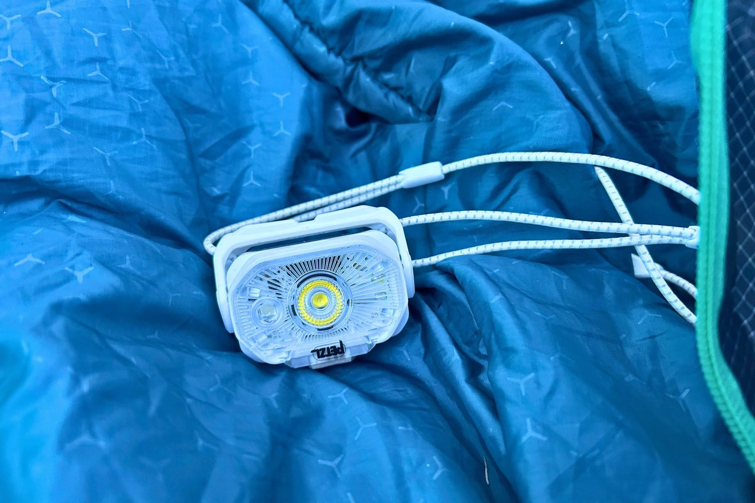 A closeup of the Petzl Swift LT headlamp. It's sitting on top of a bright blue sleeping bag.