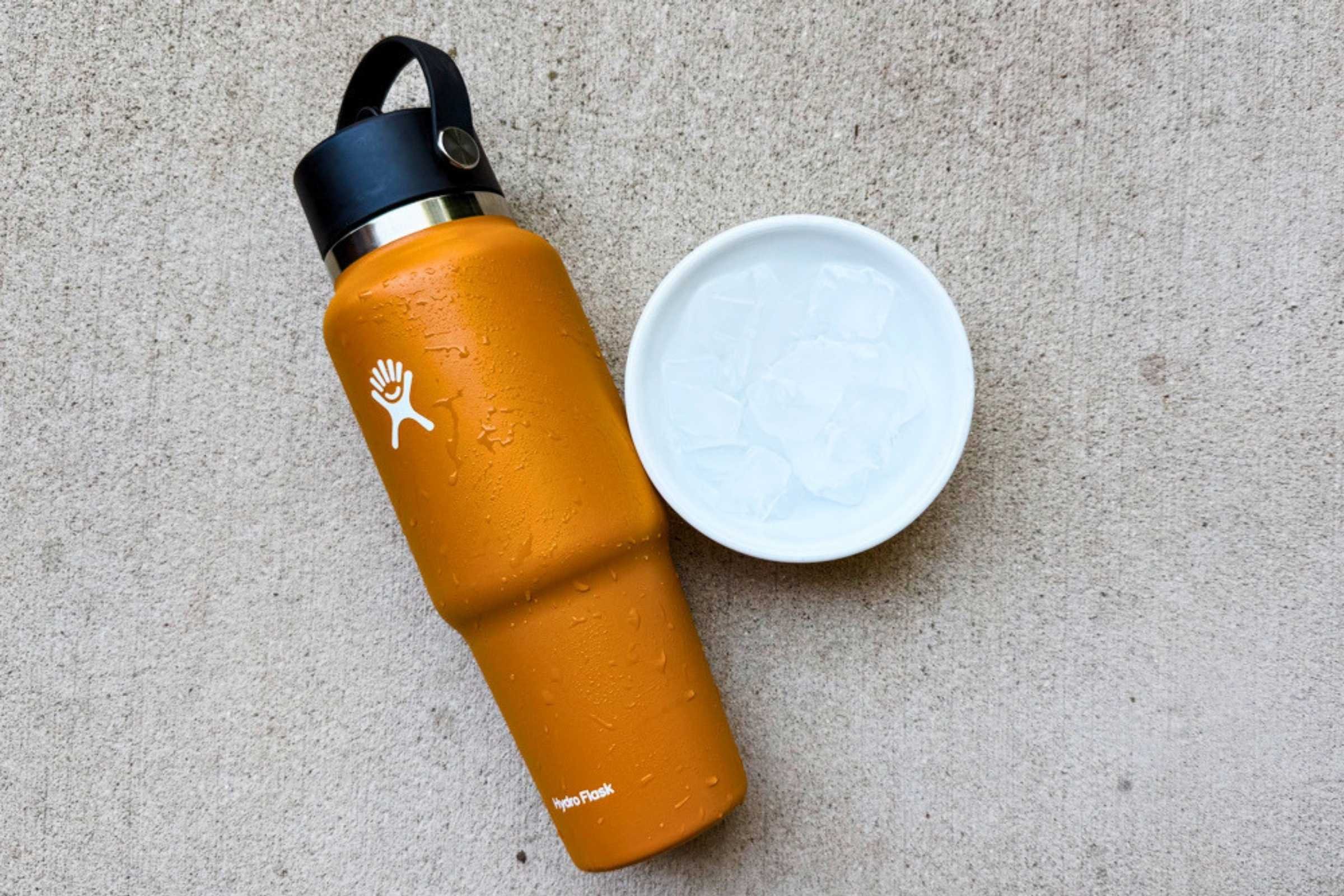 Orange Hydro Flask bottle with black straw lid beside a cup of ice.