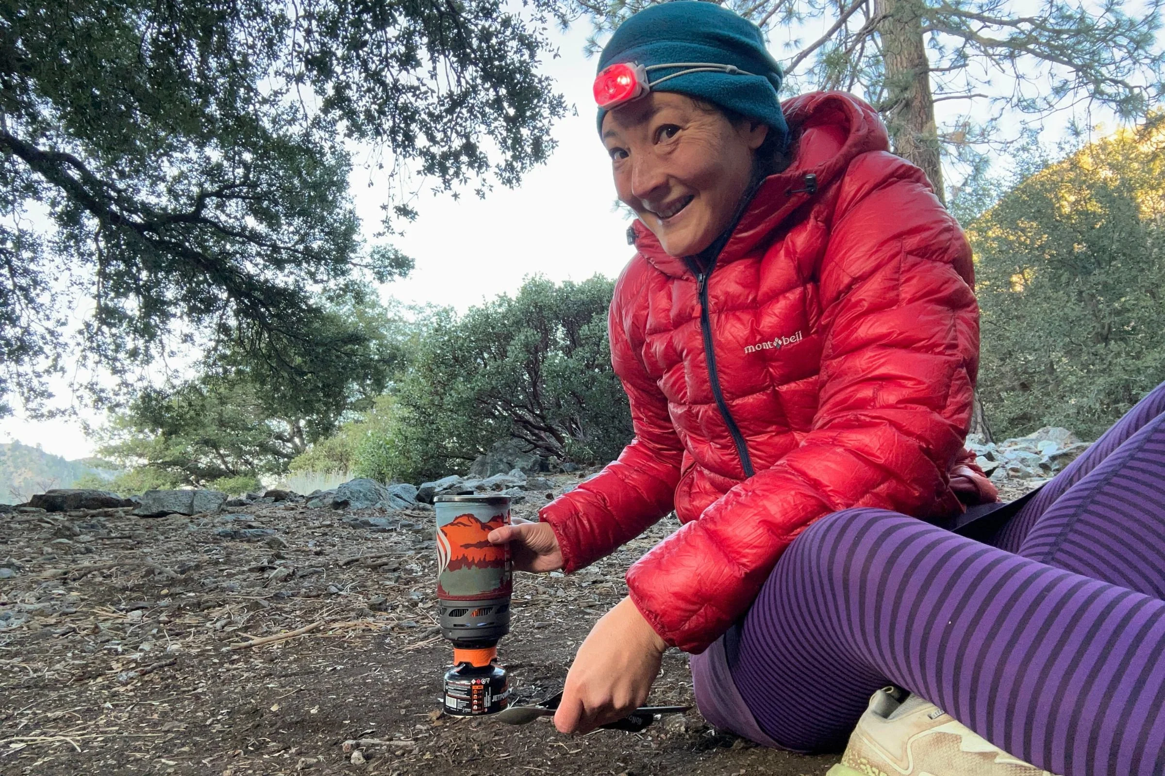 The author wearing the Petzl Swift LT headlamp in camp while cooking, with trees and rocks in the background.