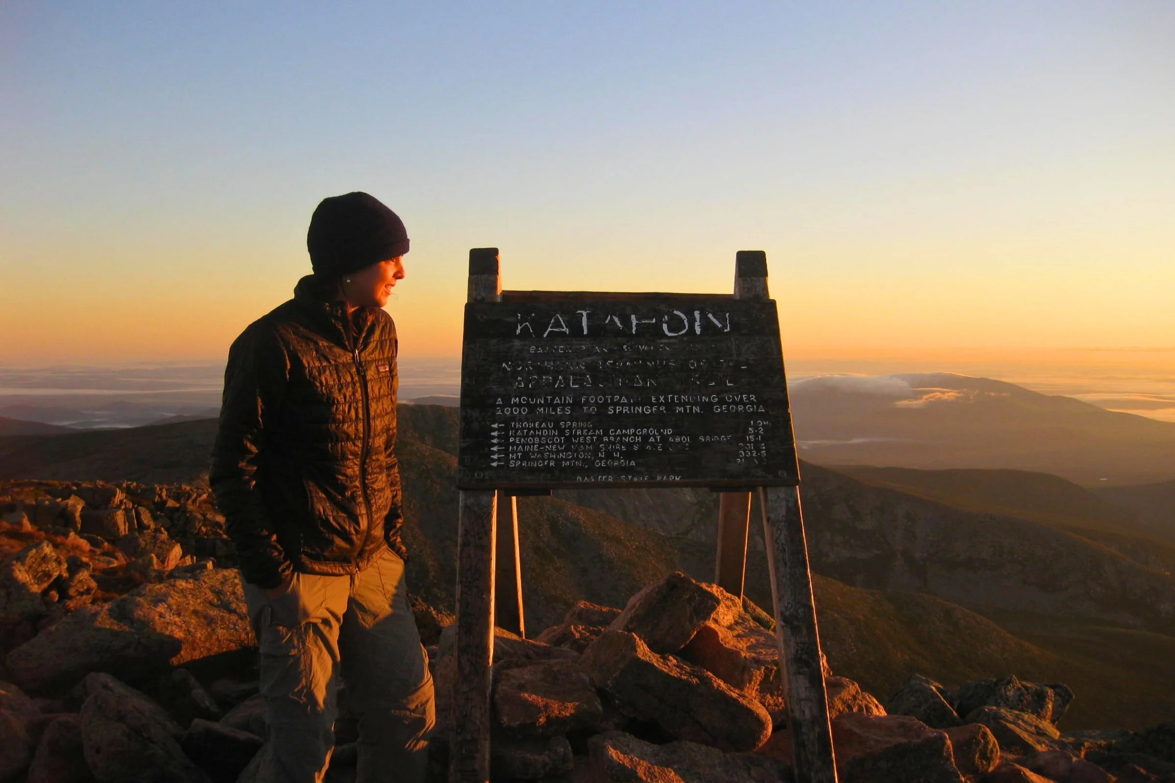 Woman wearing Patagonia Nano Puff jacket, standing next to the Katahdin Trail sign.
