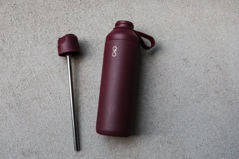 a magenta ocean go water bottle with the lid/straw laying beside it