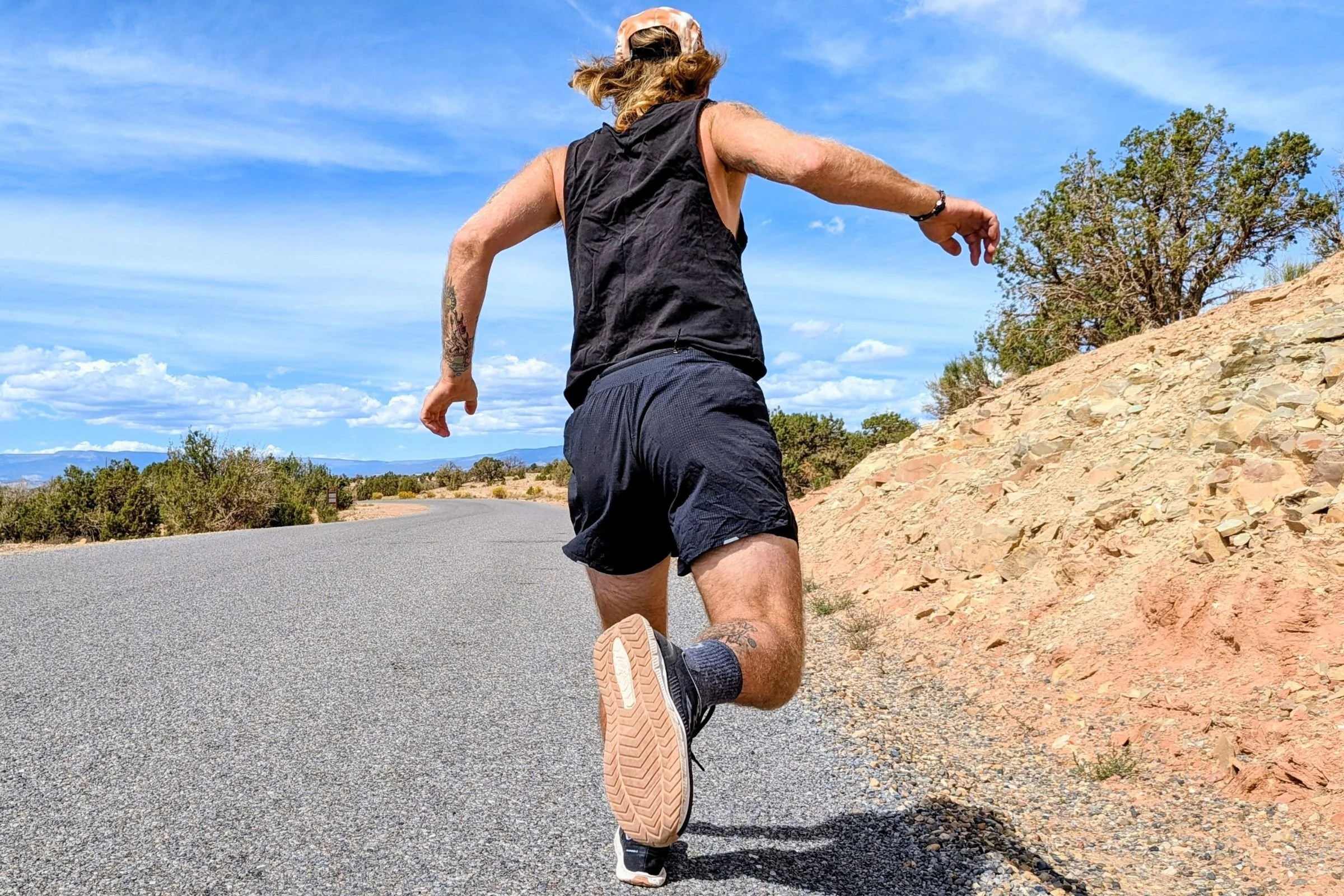 Runner wearing Lems ZENSPEED+ shoes with arms outstretched on a road.