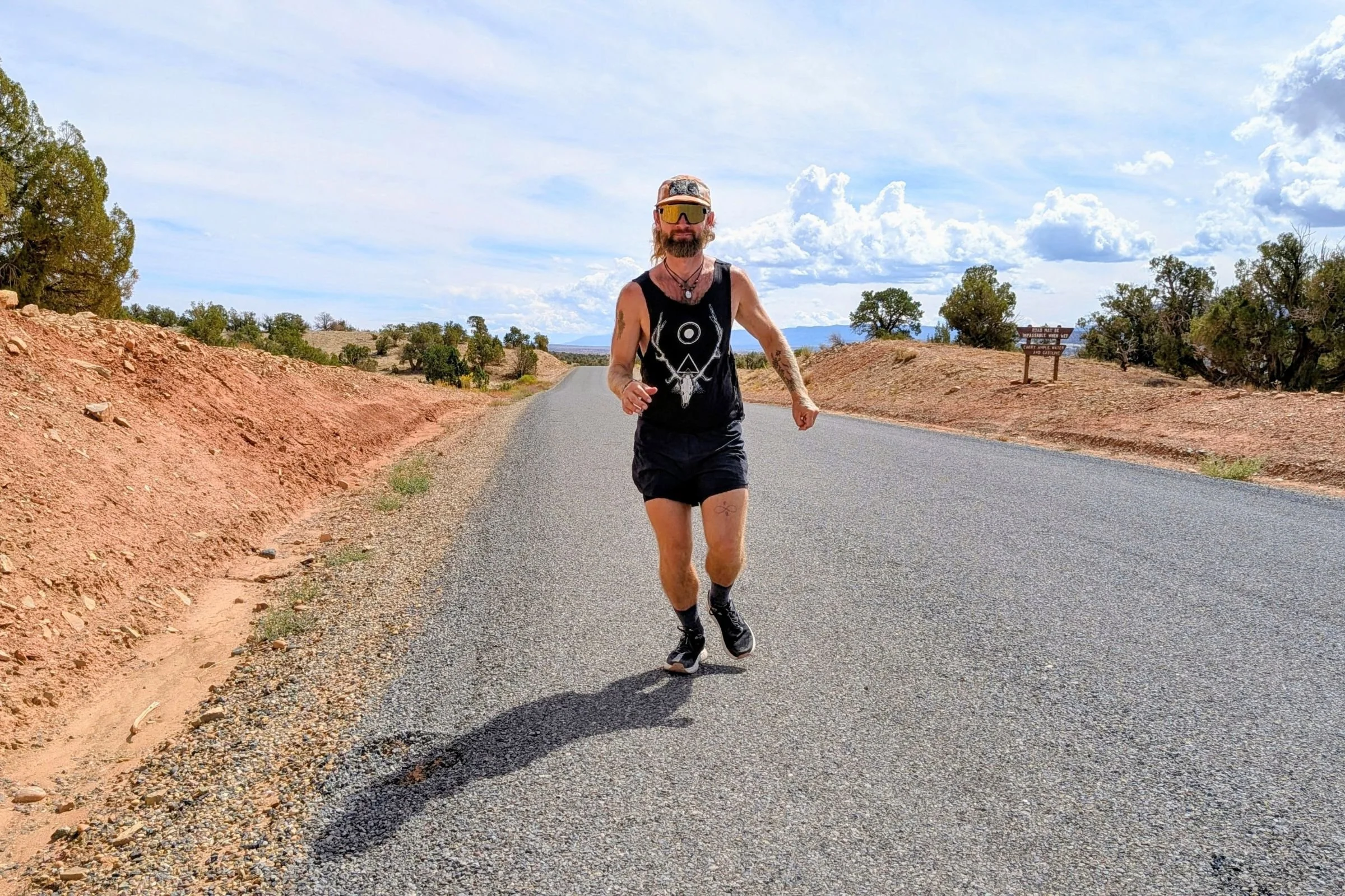 Runner in a black tank top and shorts wearing Lems ZENSPEED+ shoes while running on a paved road.