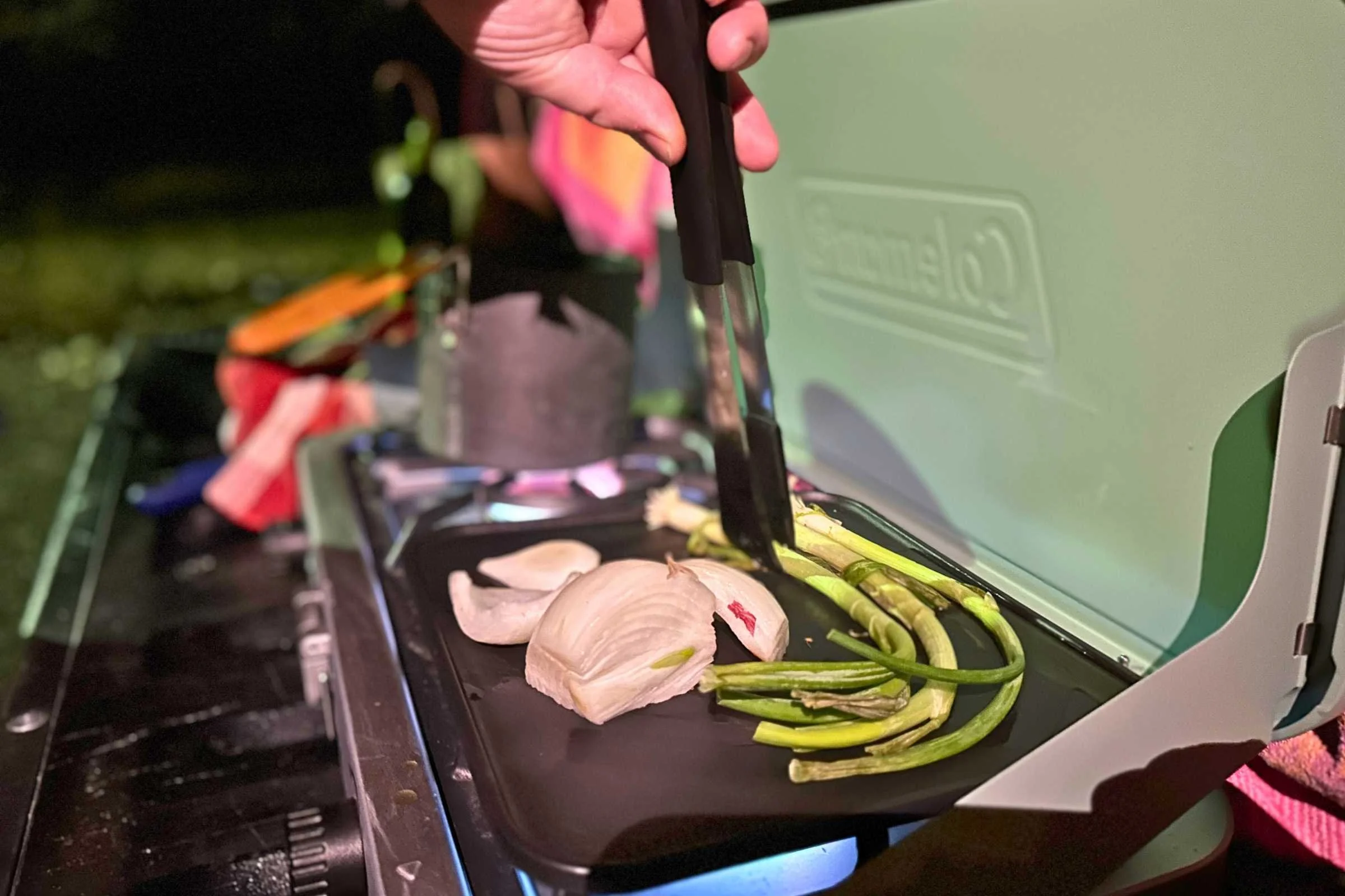 Food cooking on cast iron grill attached to Coleman Cascade stove