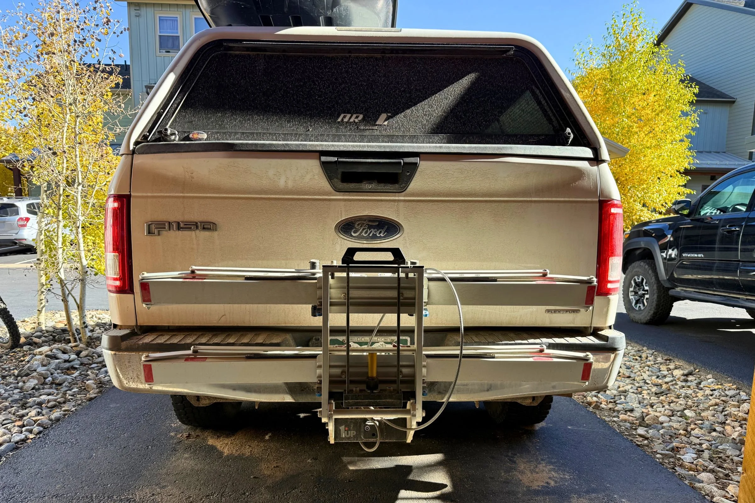 Truck with a trailer attached, showing the 1UP USA Heavy Duty Hitch Bike Rack folded and empty.