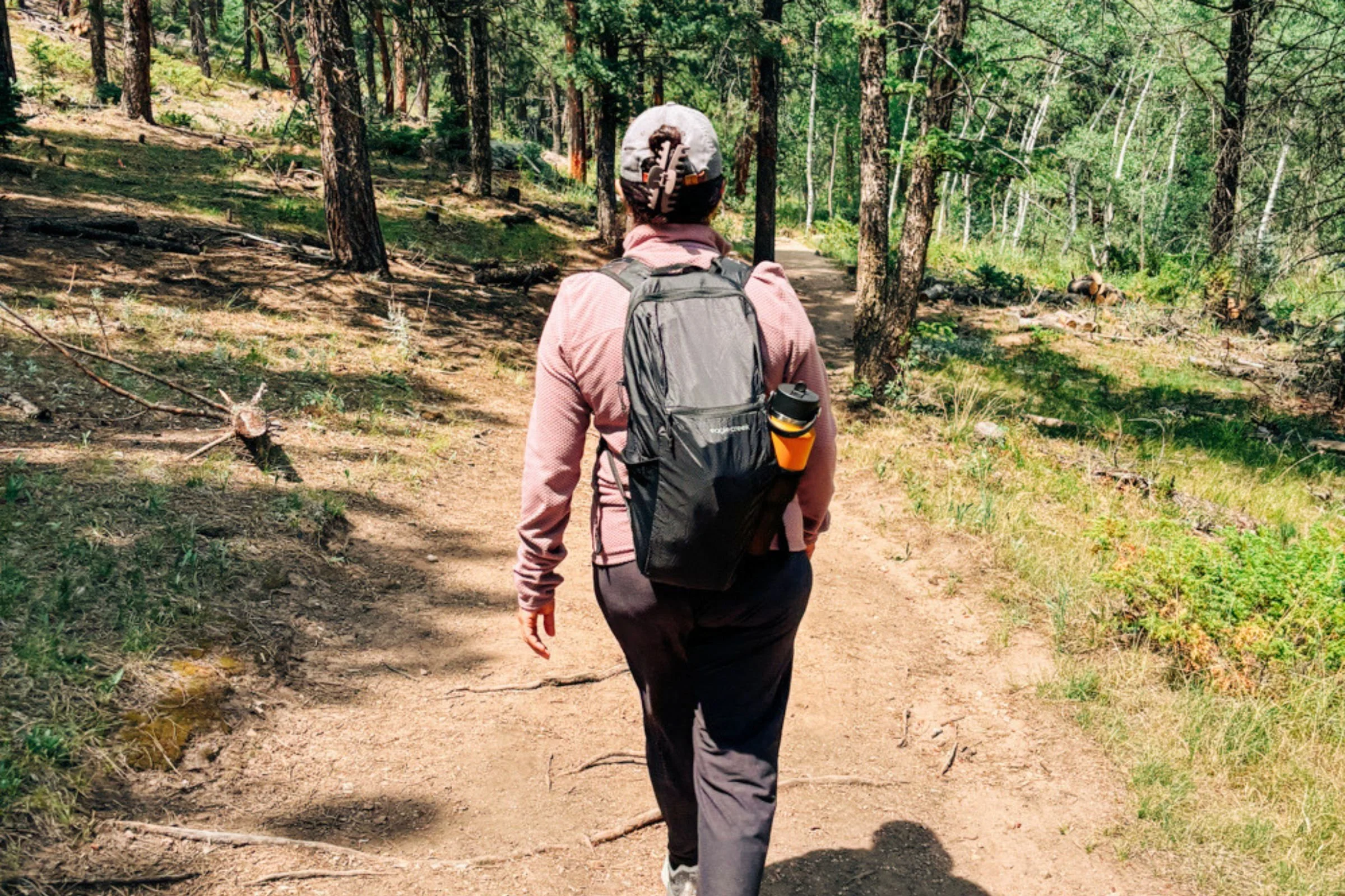 Woman wearing a black Eagle Creek Packable Backpack while walking along a trail.