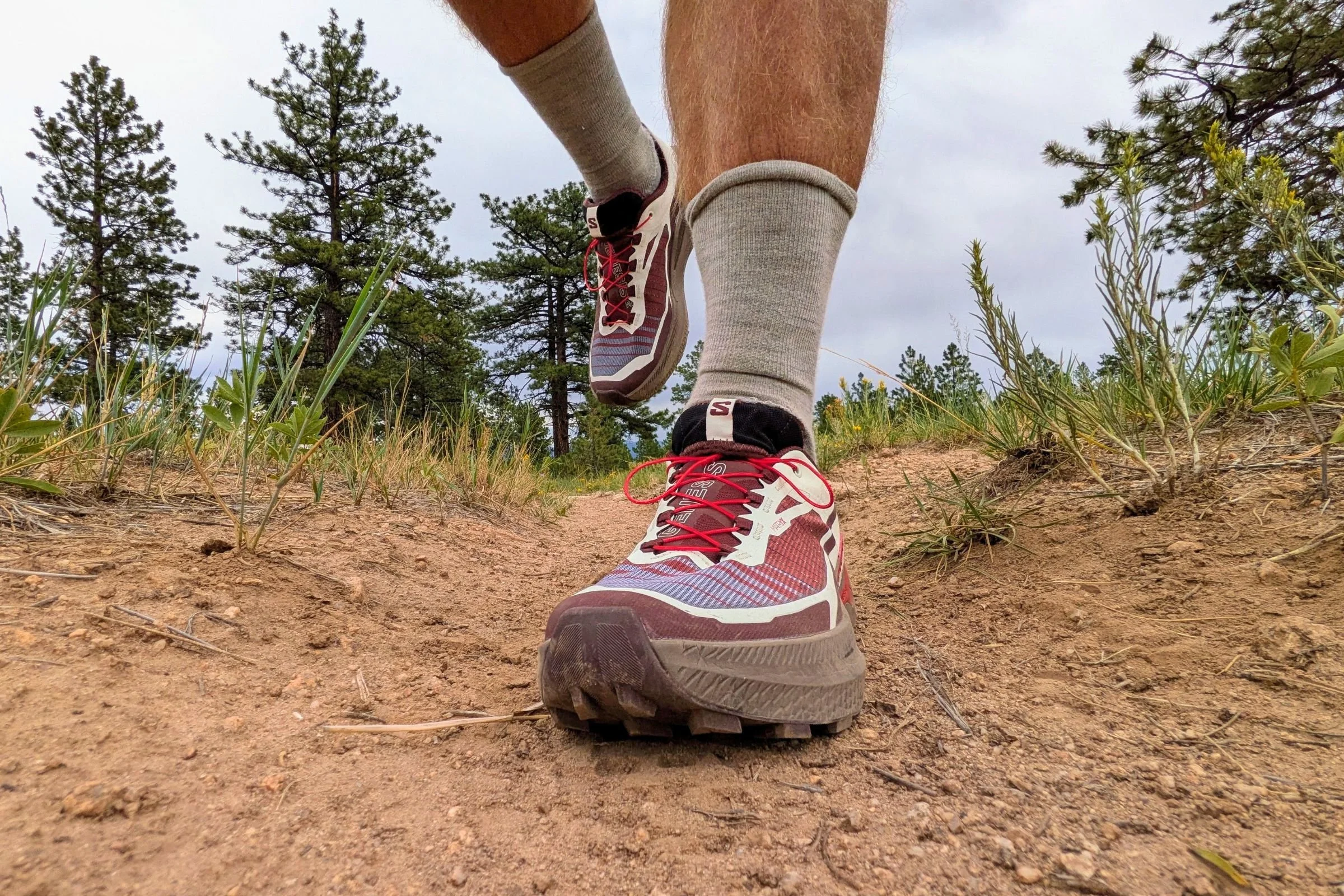 A man wearing Salomon Genesis 2 Trail Running Shoes runs along a dirt trail outdoors.