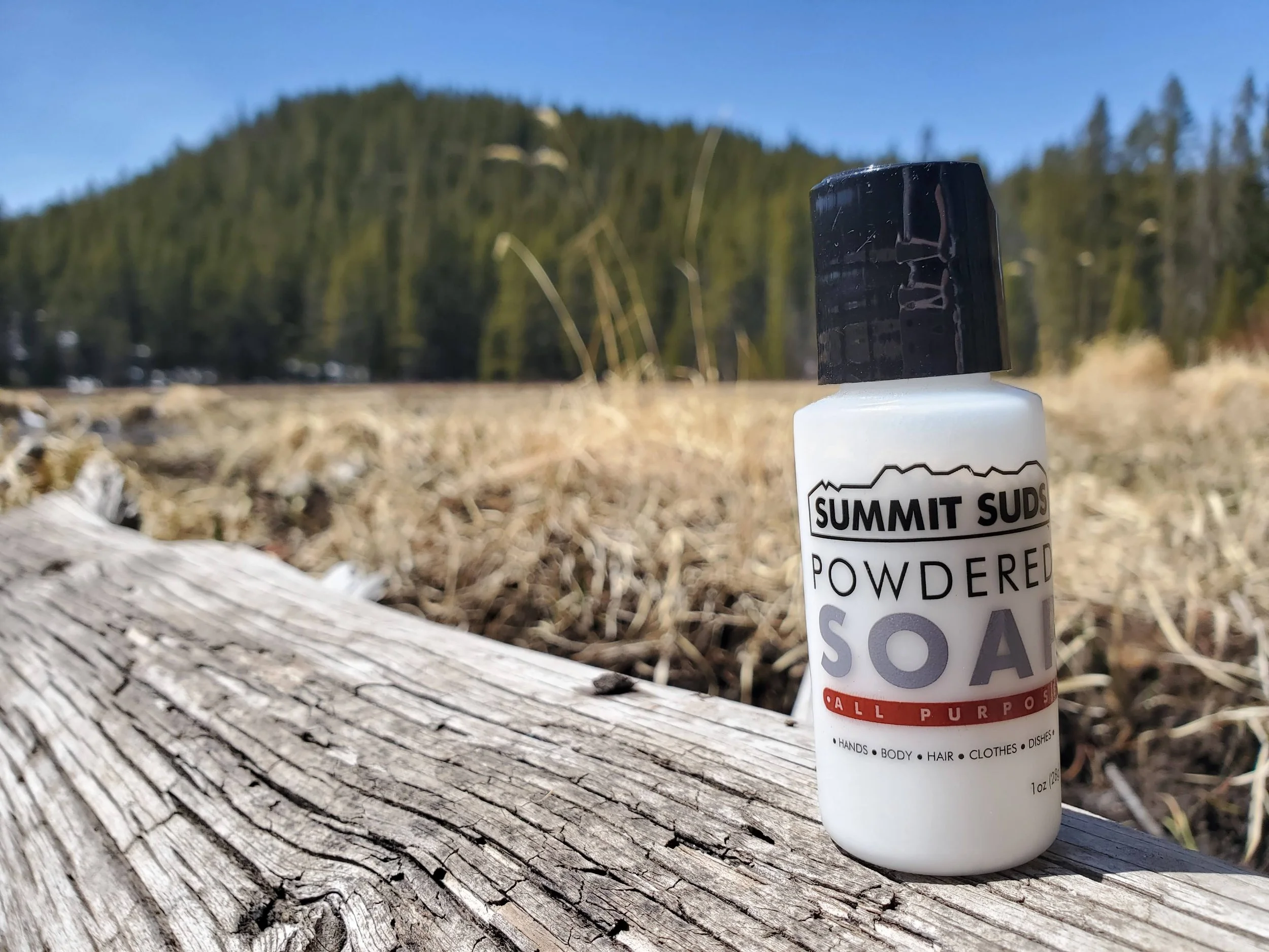 A small bottle of summit suds powdered soap on a log