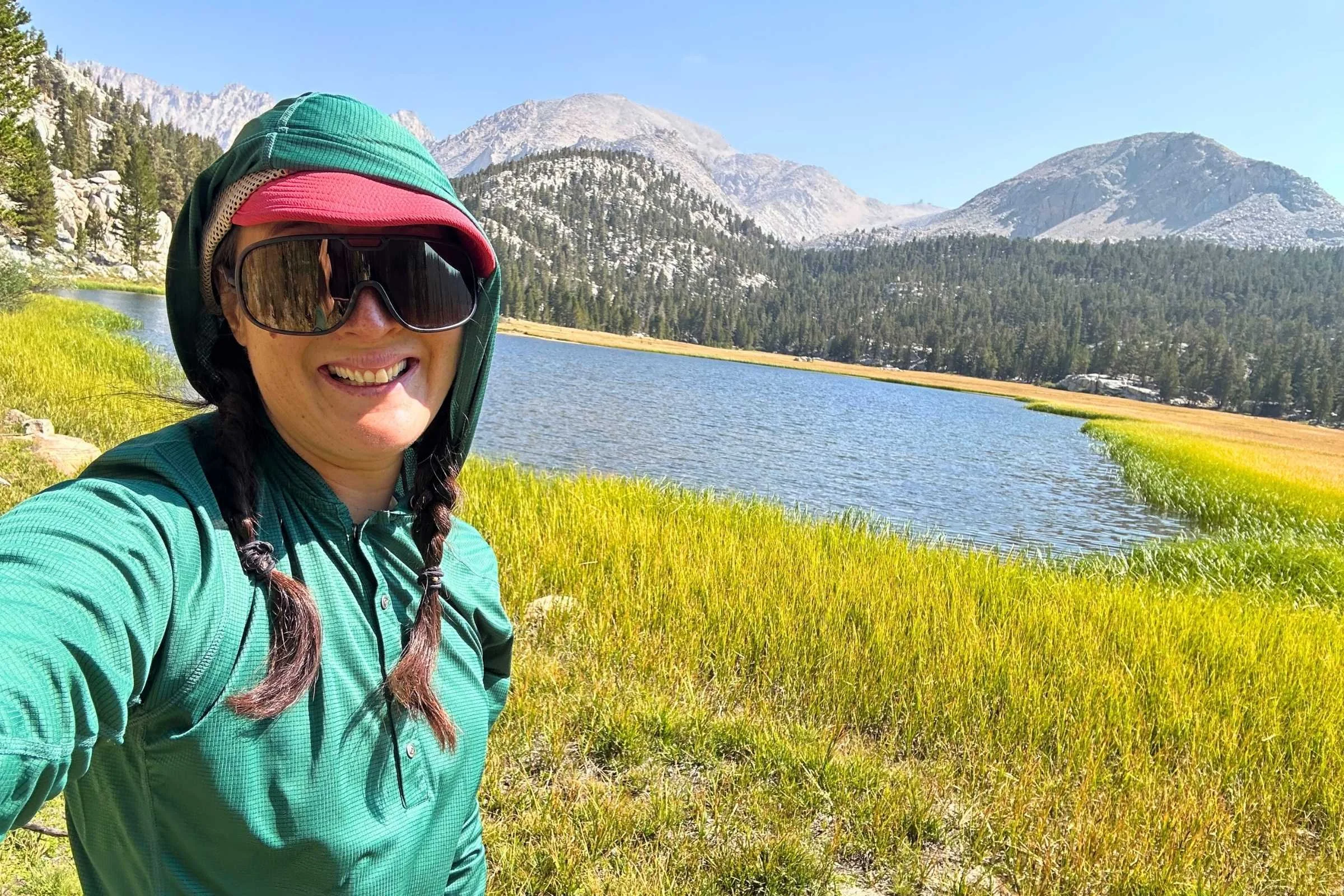 Woman wearing Zpacks Sun Hoodie beside alpine lake with mountains in the background