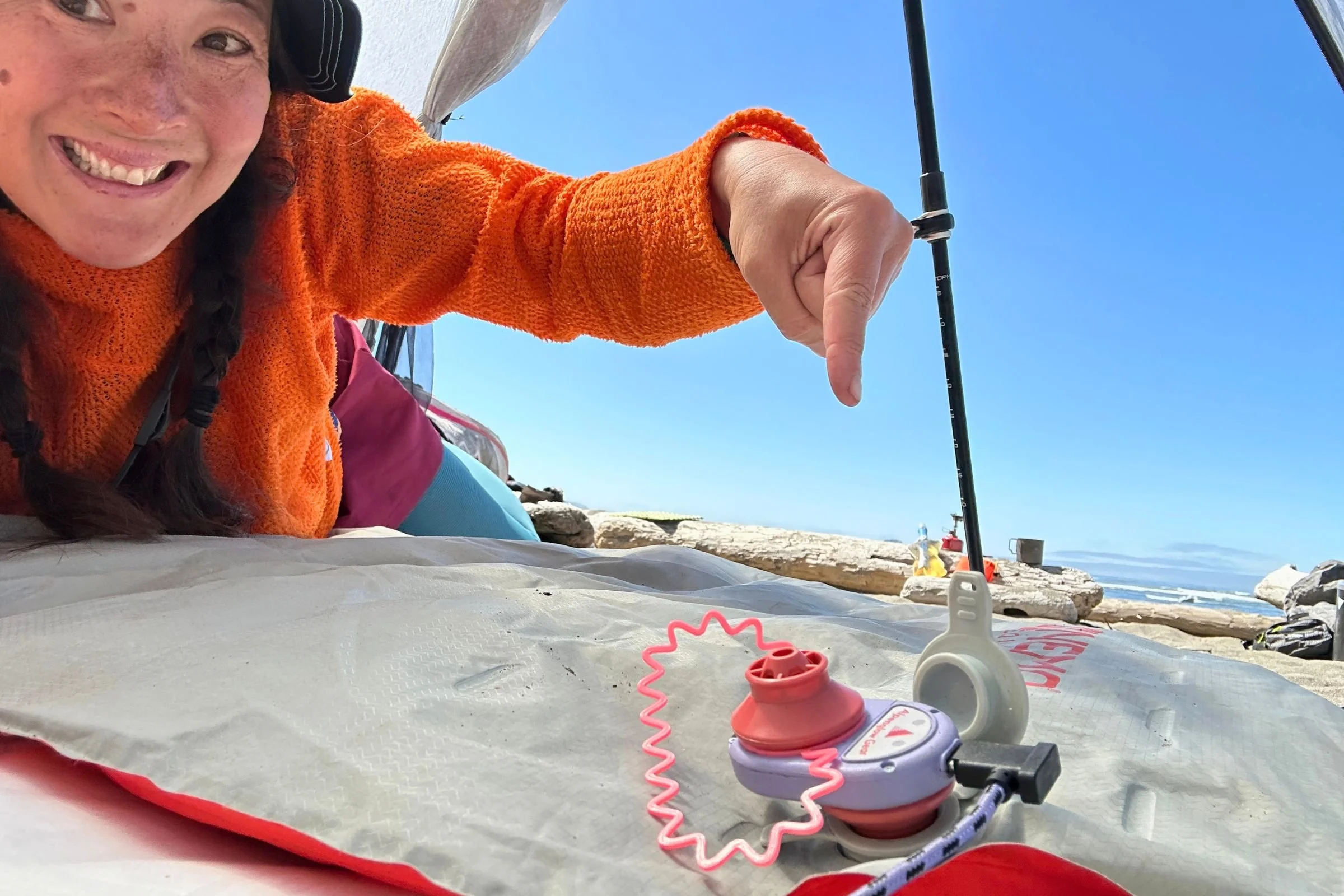 Treeline Review Editor-in-Chief Liz Thomas points to an Alpenglow sleeping pad inflator connected to a sleeping pad at a coastal campsite.