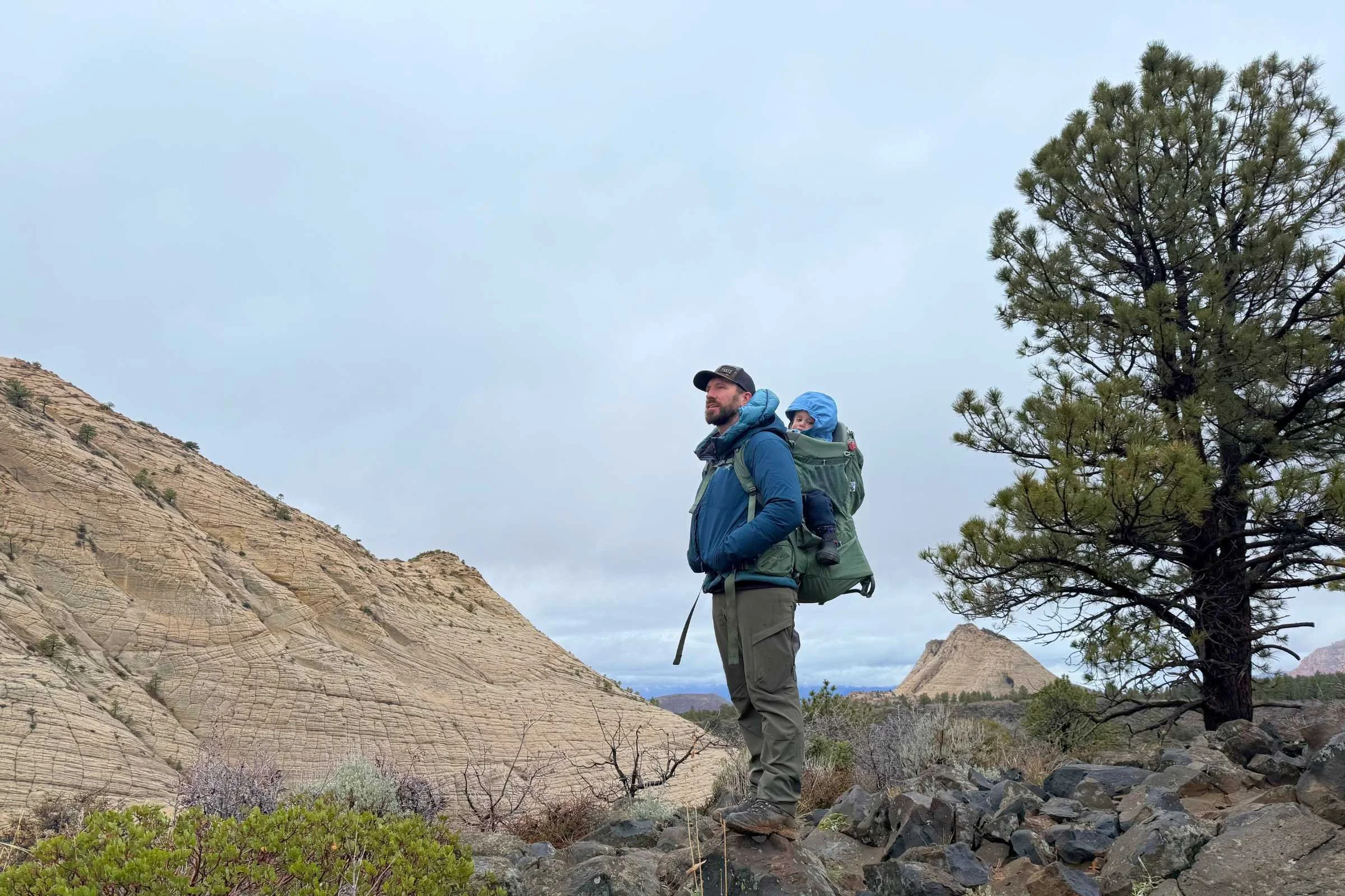 Man hiking with child carrier wearing KUIU Attack pants on rocky trail