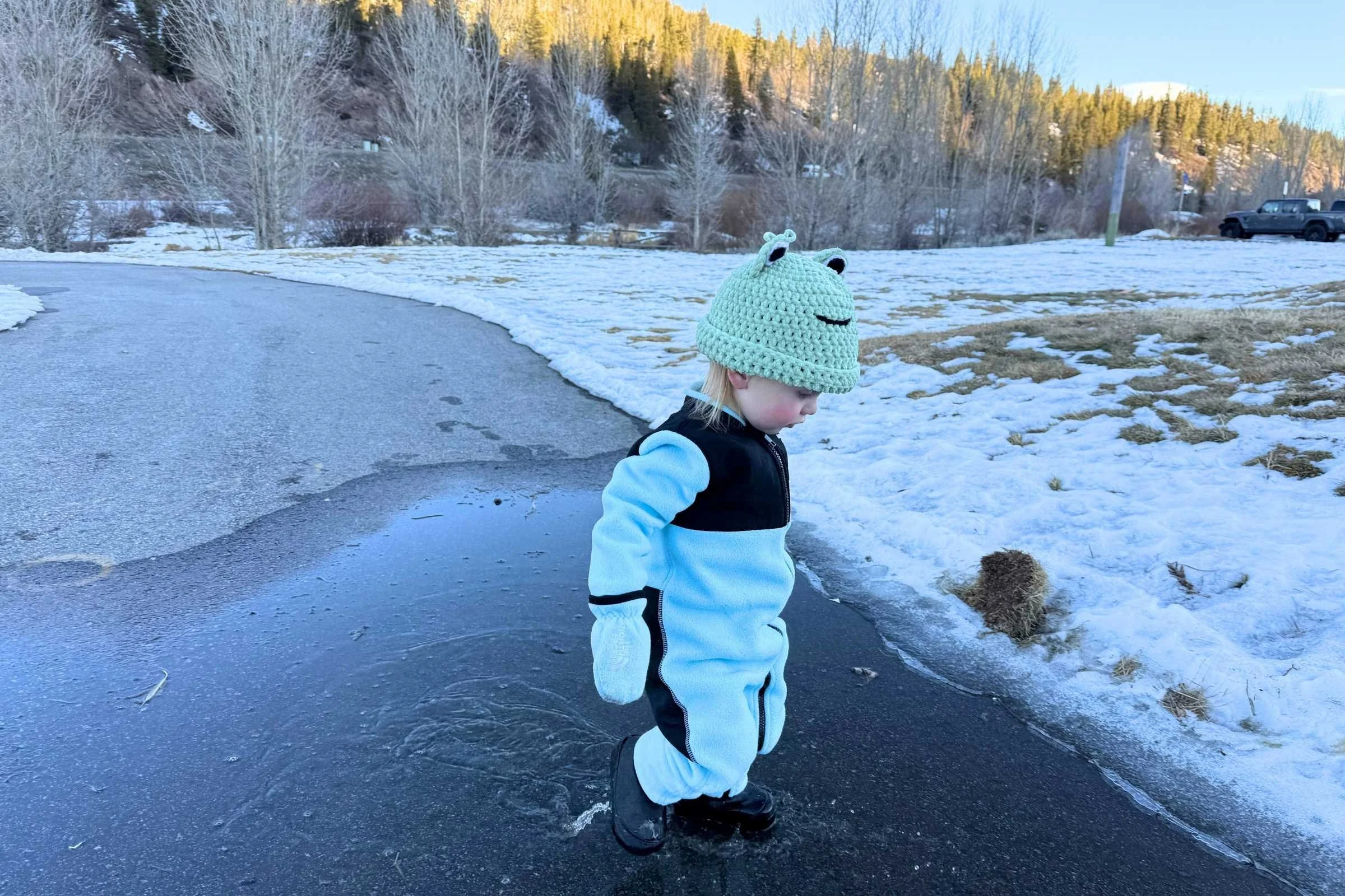Toddler wearing winter boots walking through icy puddle on snowy path