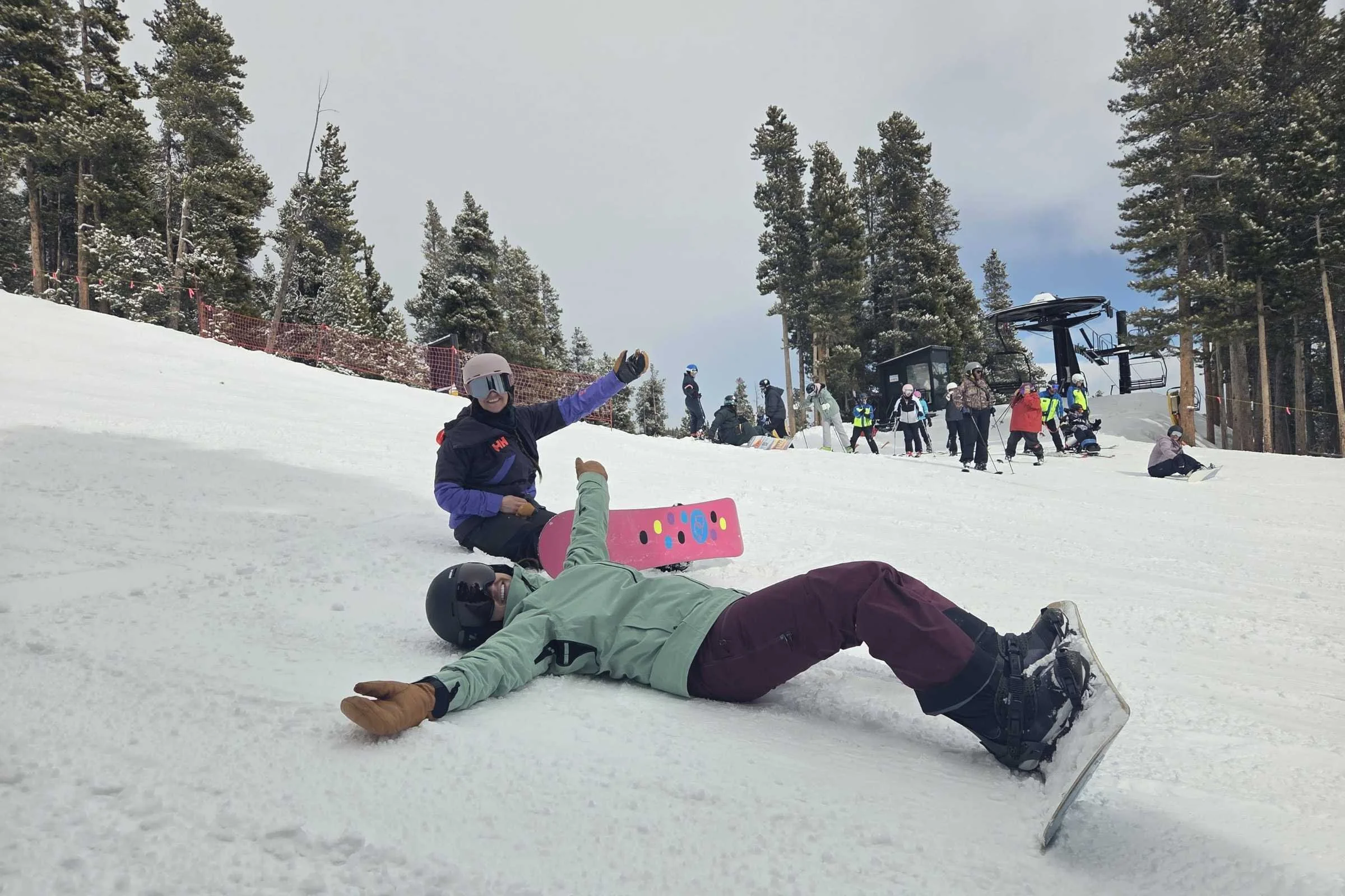 two snowboarders laying on the side of the slope