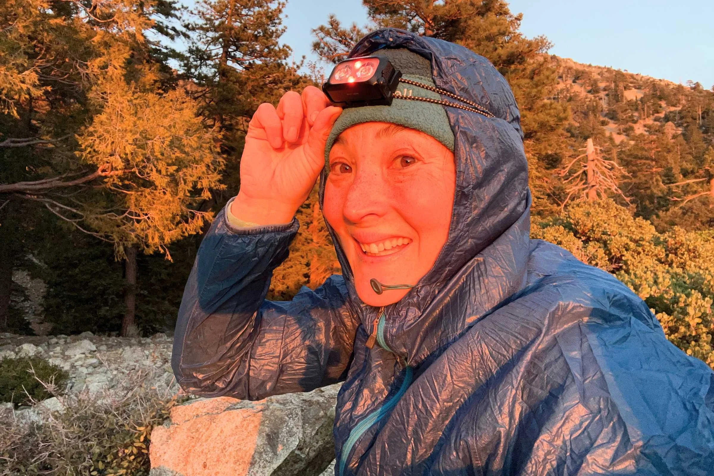 Bundled-up hiker wearing the Nitecore NU25 MCT headlamp in red-light mode with early morning sun on their face.