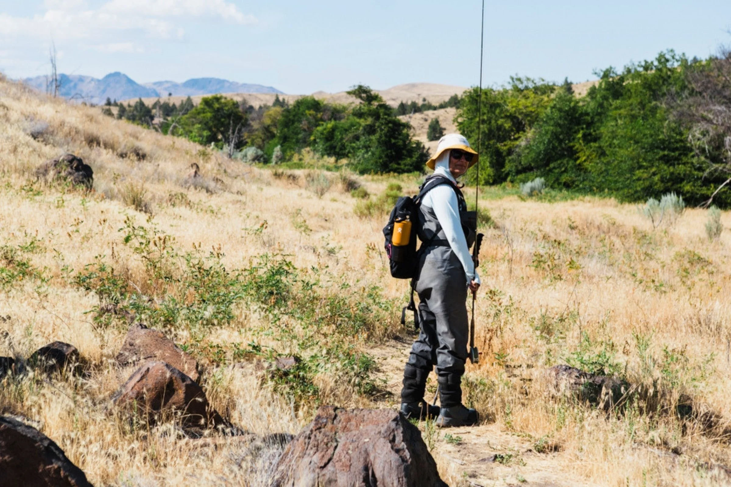 Person with a backpack holding a Hydro Flask 32 oz Travel Bottle on a trail.