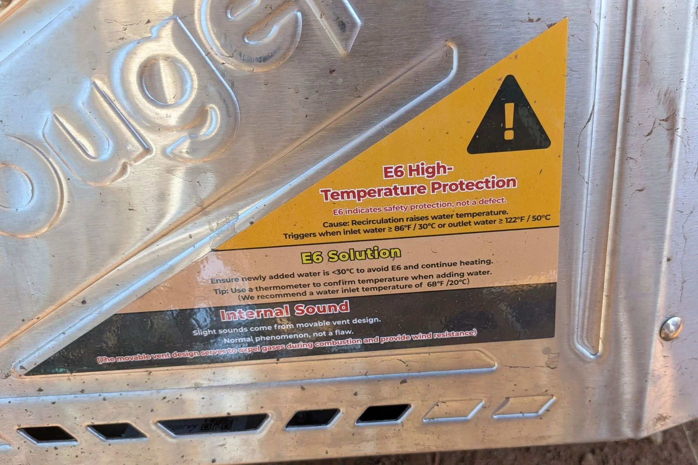 A close-up of the metal unit with a warning label on the BougeRV Portable Propane Outdoor Water Heater.