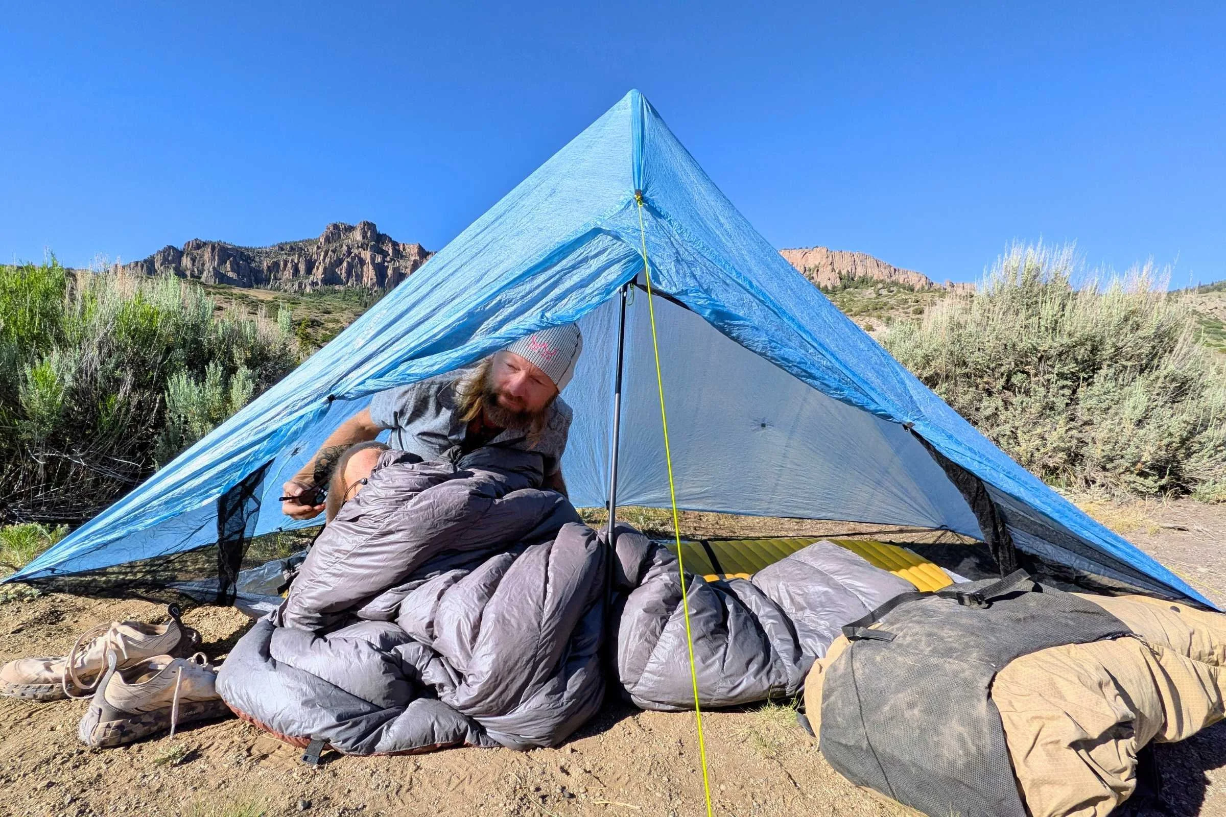 The author in a tent arranging with Outdoor Vitals StormLoft 15 Quilt with shrubs and mountains in the background