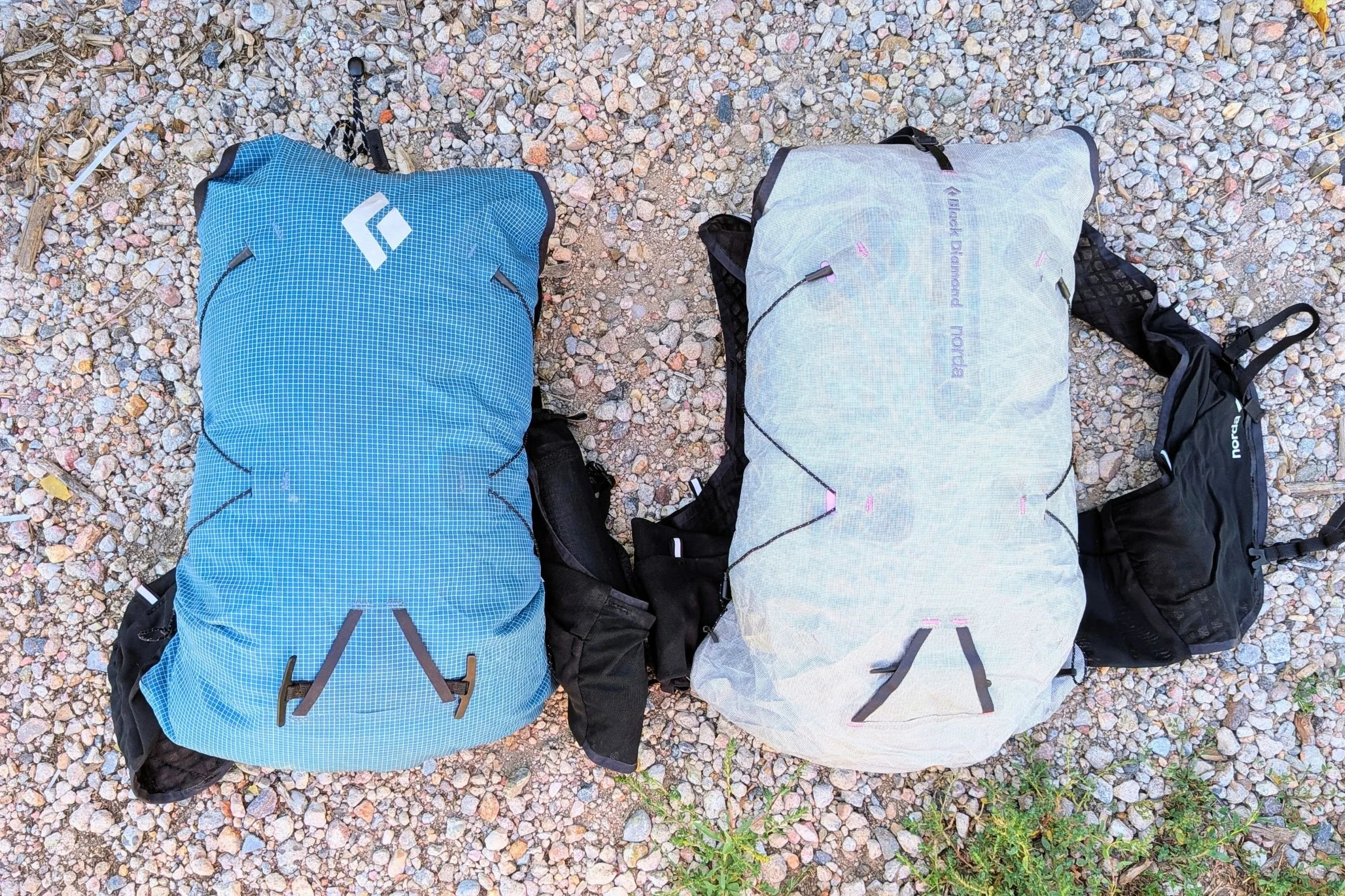 Blue standard and gray norda collaboration Black Diamond Distance 15 Backpacks lying side by side on gravel