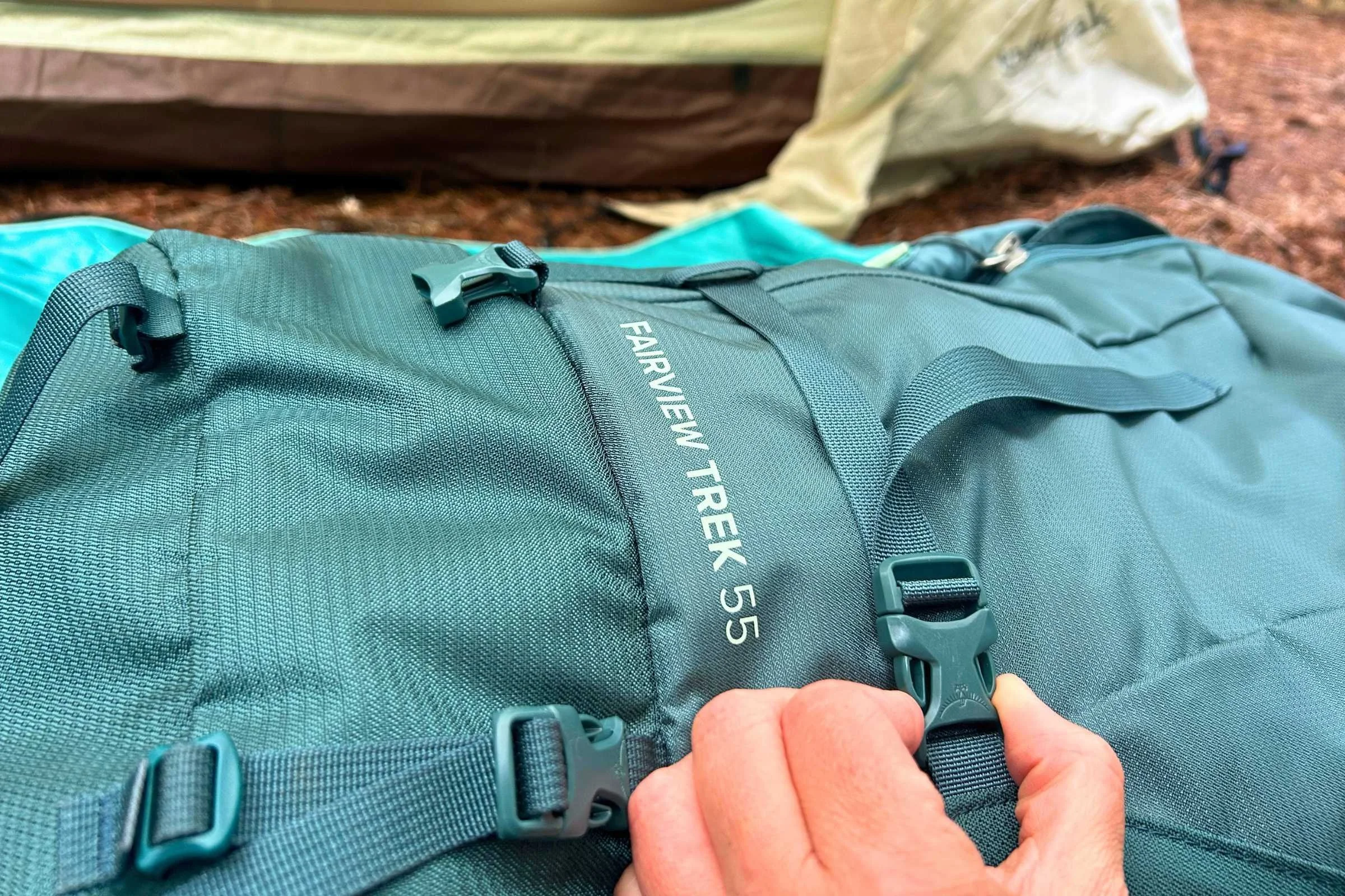 Person holding the Osprey Fairview Trek 55 Travel Pack with a tent in the background.