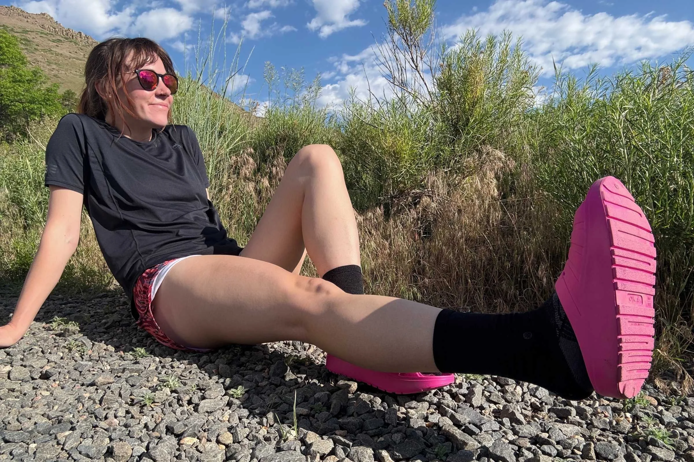 Woman sitting on a gravel trail wearing pink Oka recovery slides