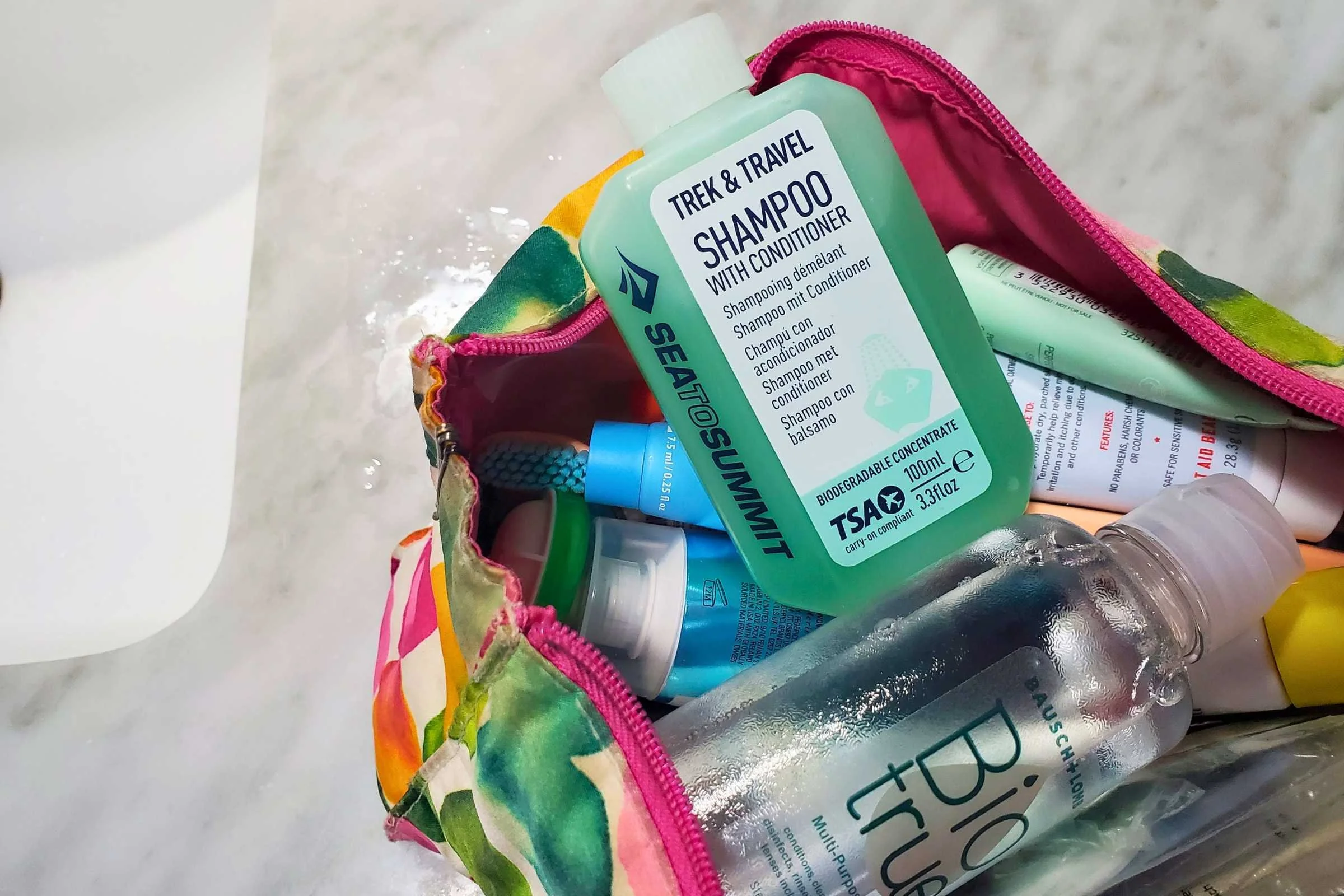 A travel-size bottle of Sea to Summit Shampoo & Conditioner sits in a colorful toiletry bag on a grey tile counter