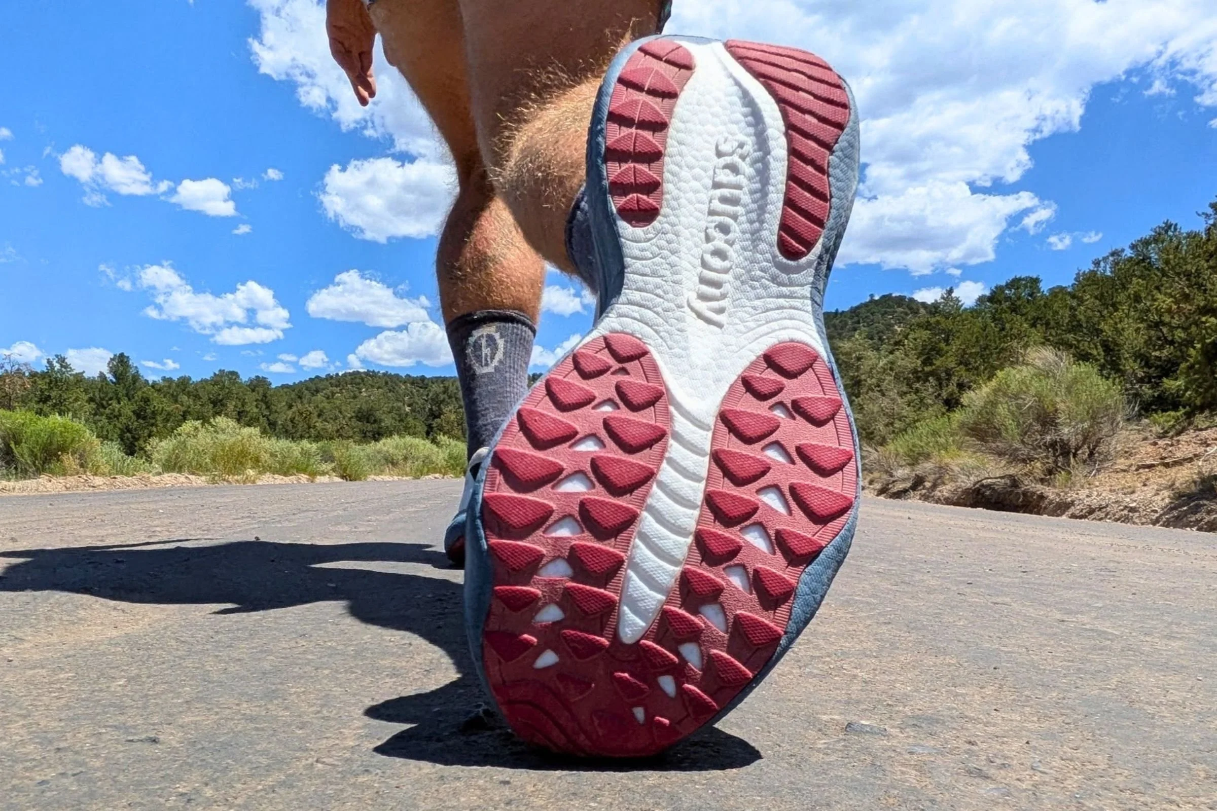 The sole of a Saucony Ride 19 Road Running Shoe with trees in the background.
